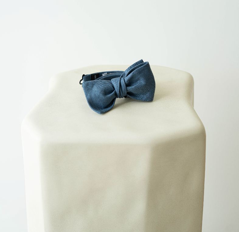 Blue denim bow on a beige cushion with a white background