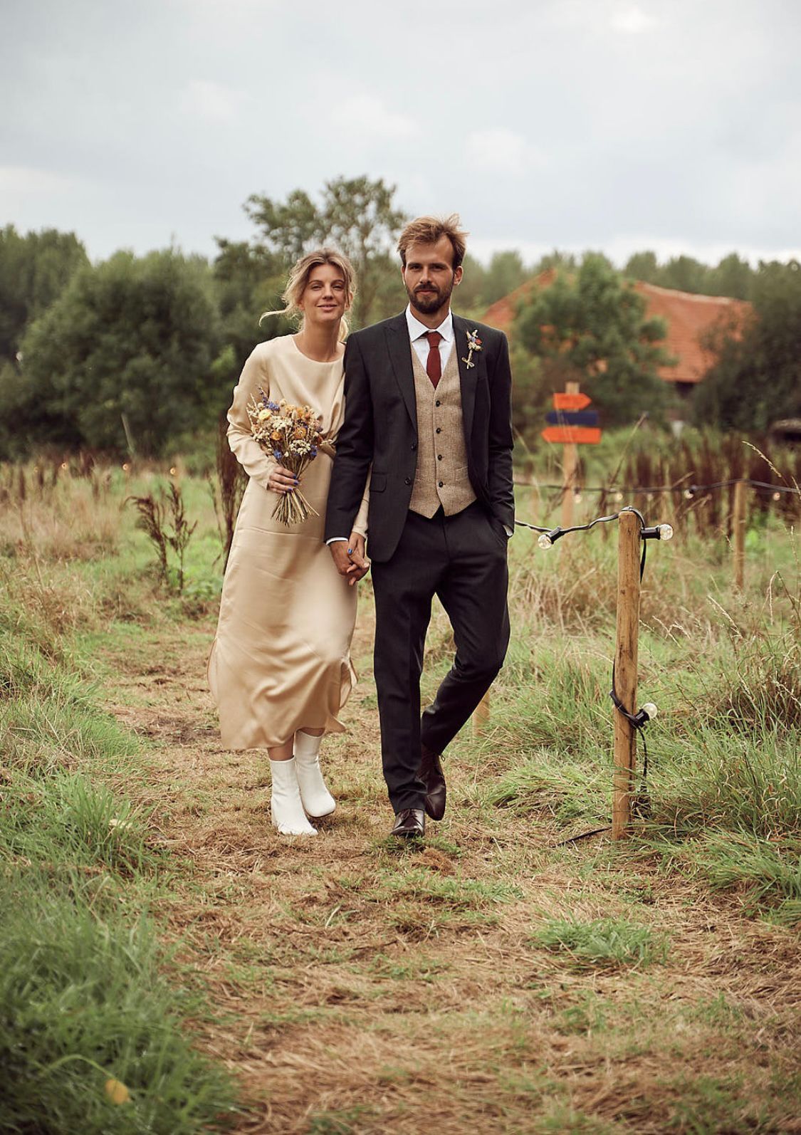 Couple walking together in a rural setting with trees and a house in the background.