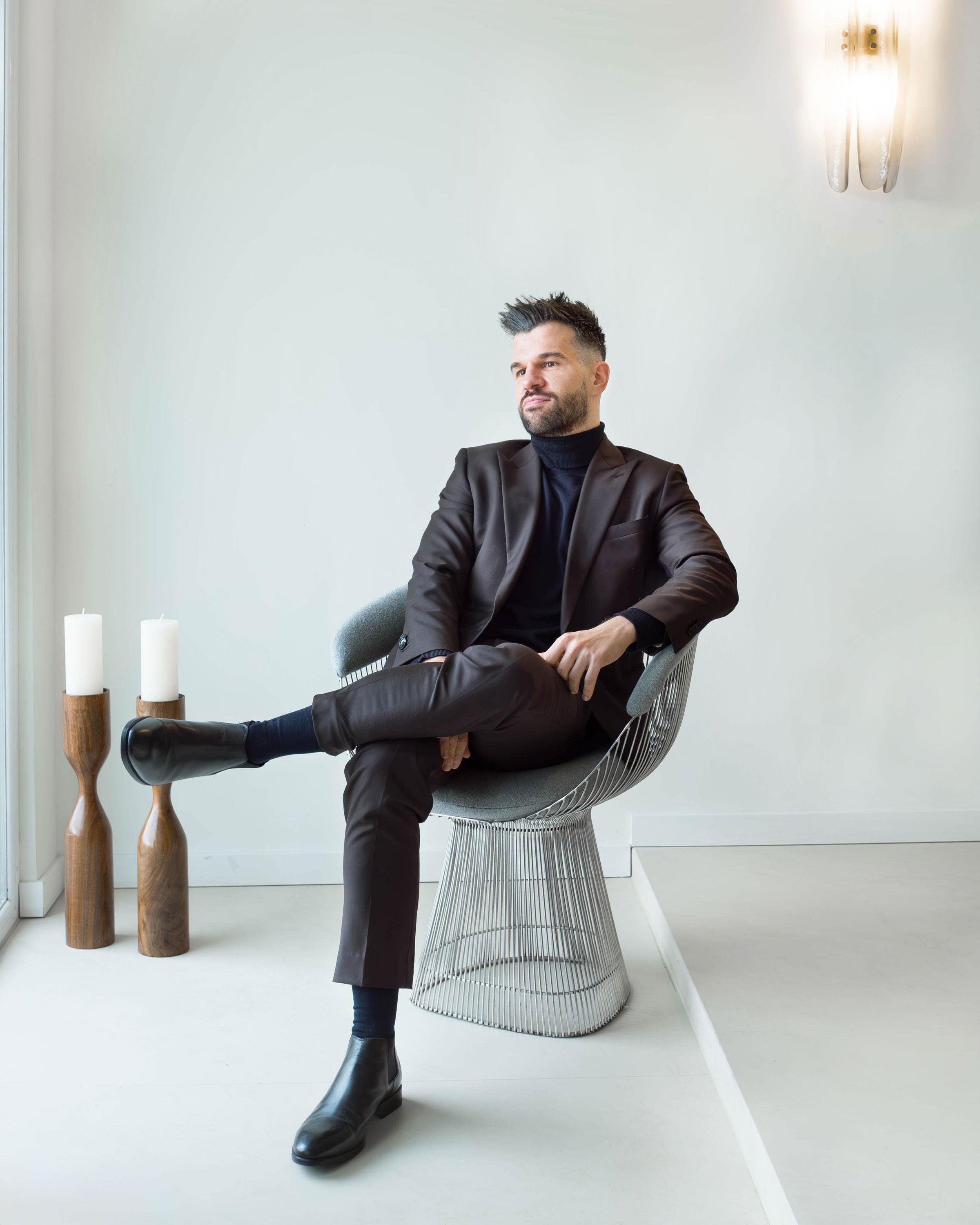 Man in a dark suit sitting on a modern chair in a minimalistic room.