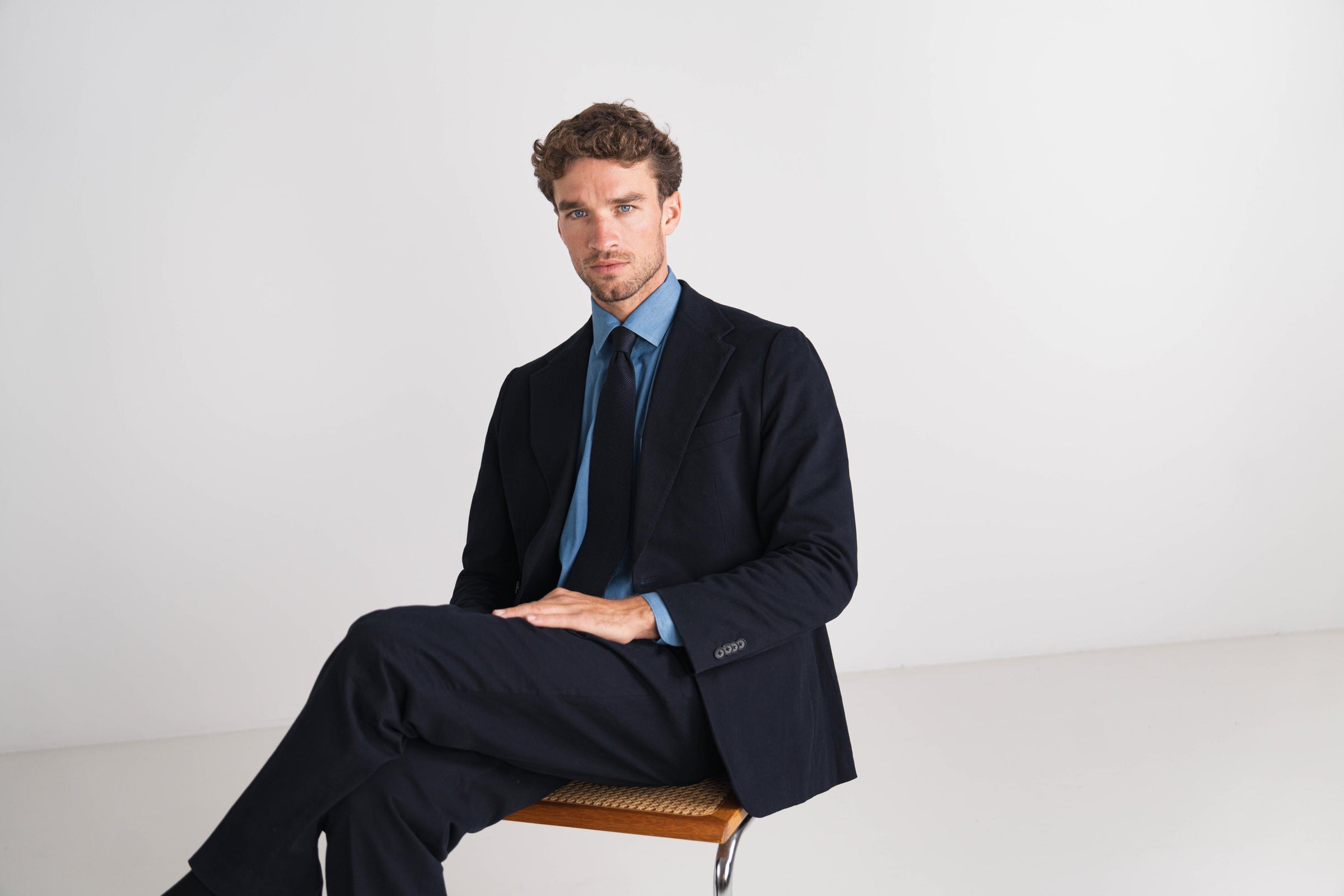 Man in a dark suit sitting on a chair against a white background