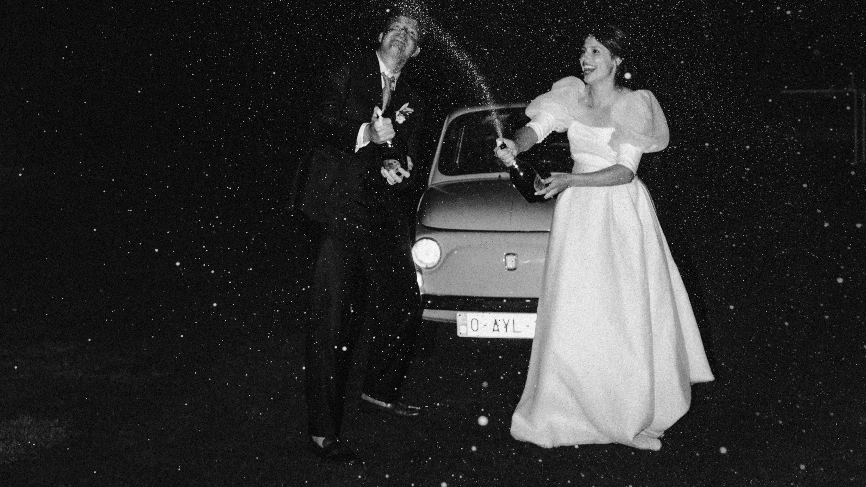 Pasgetrouwd koppel, bruidegom in tuxedo en bruid in jurk, bij een wagen onder de sterren