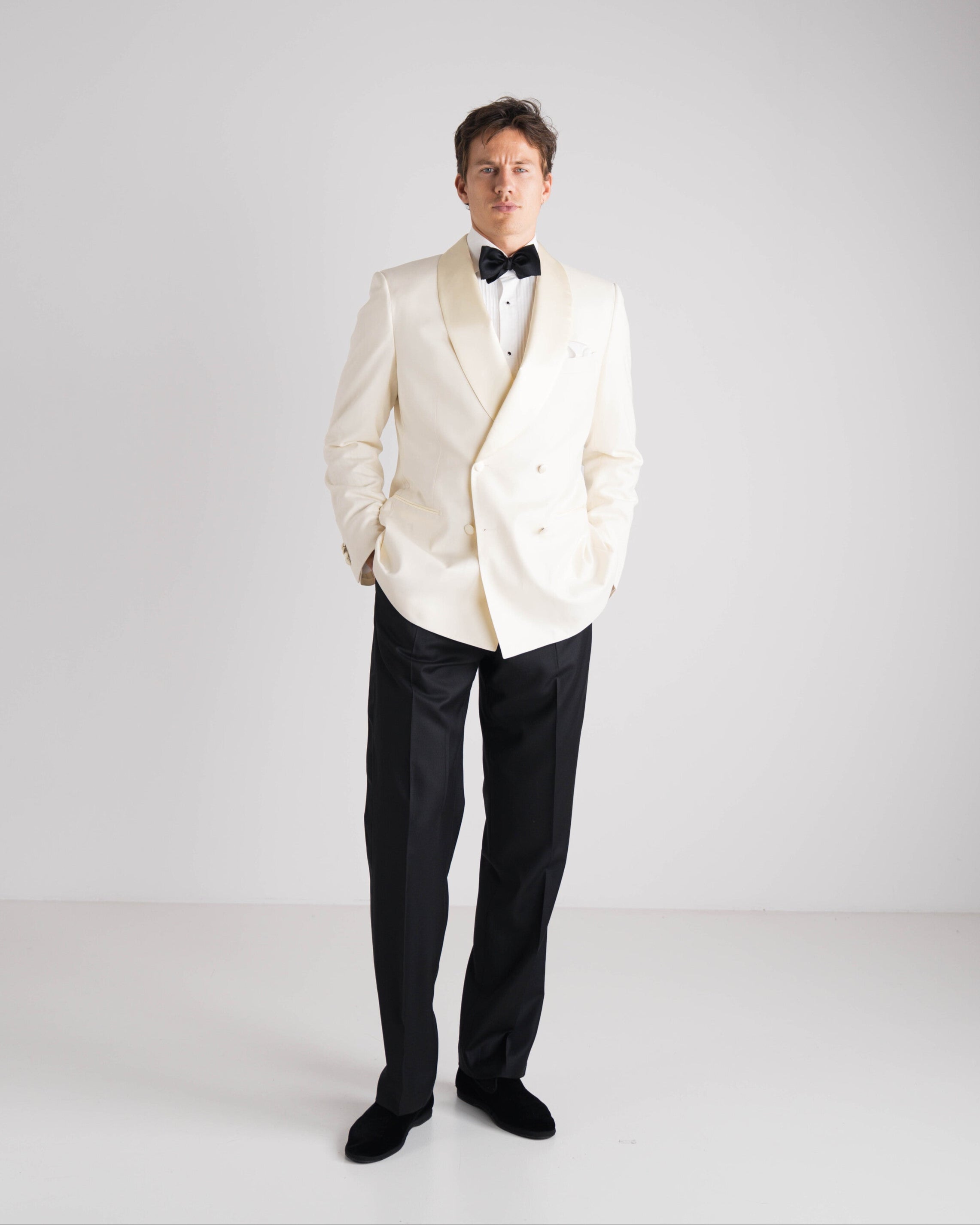 staande man in ivory double breasted tuxedo jasje en zwarte strik met zwarte broek