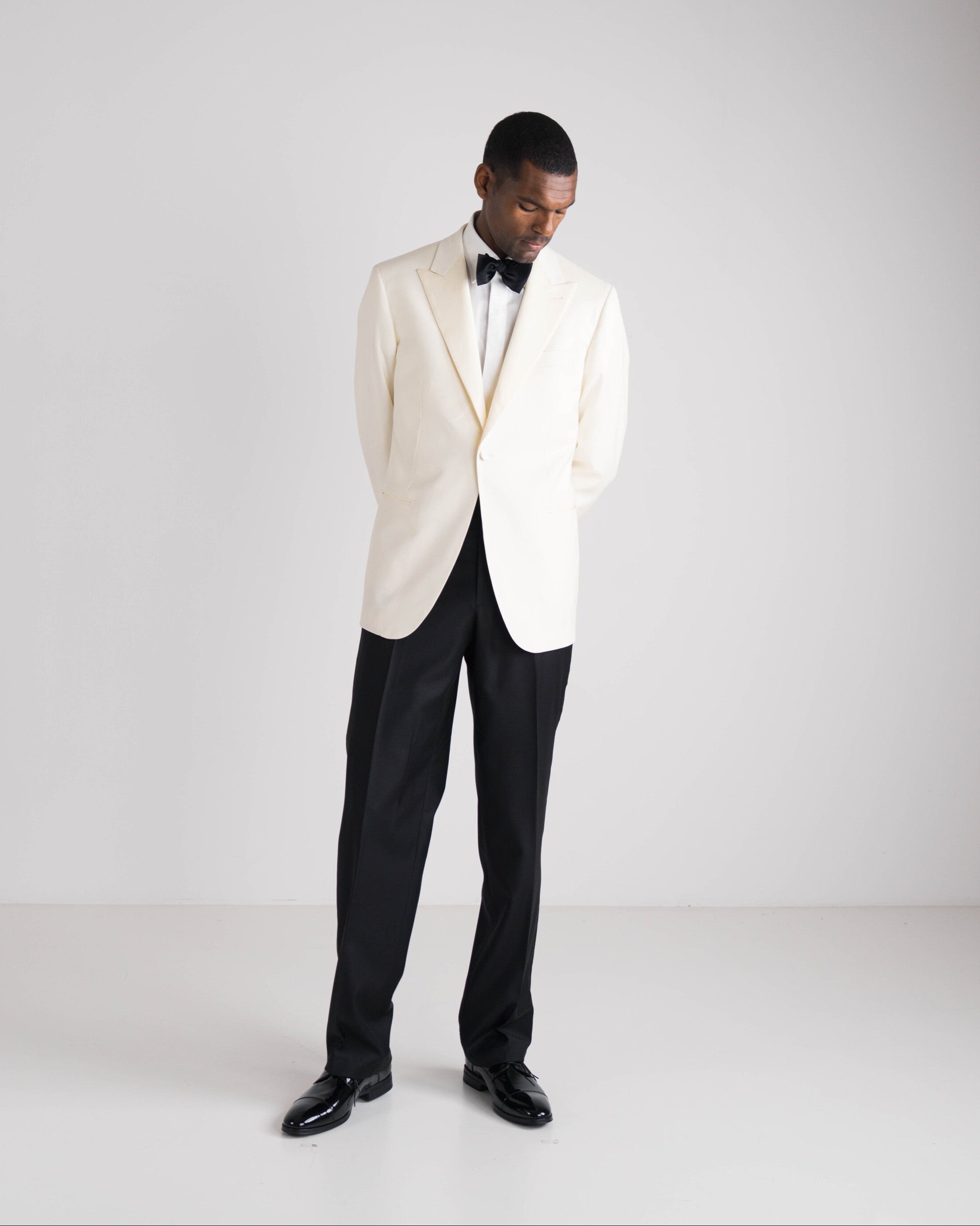 staande man in ivory tuxedo jasje en zwarte strik met zwarte broek