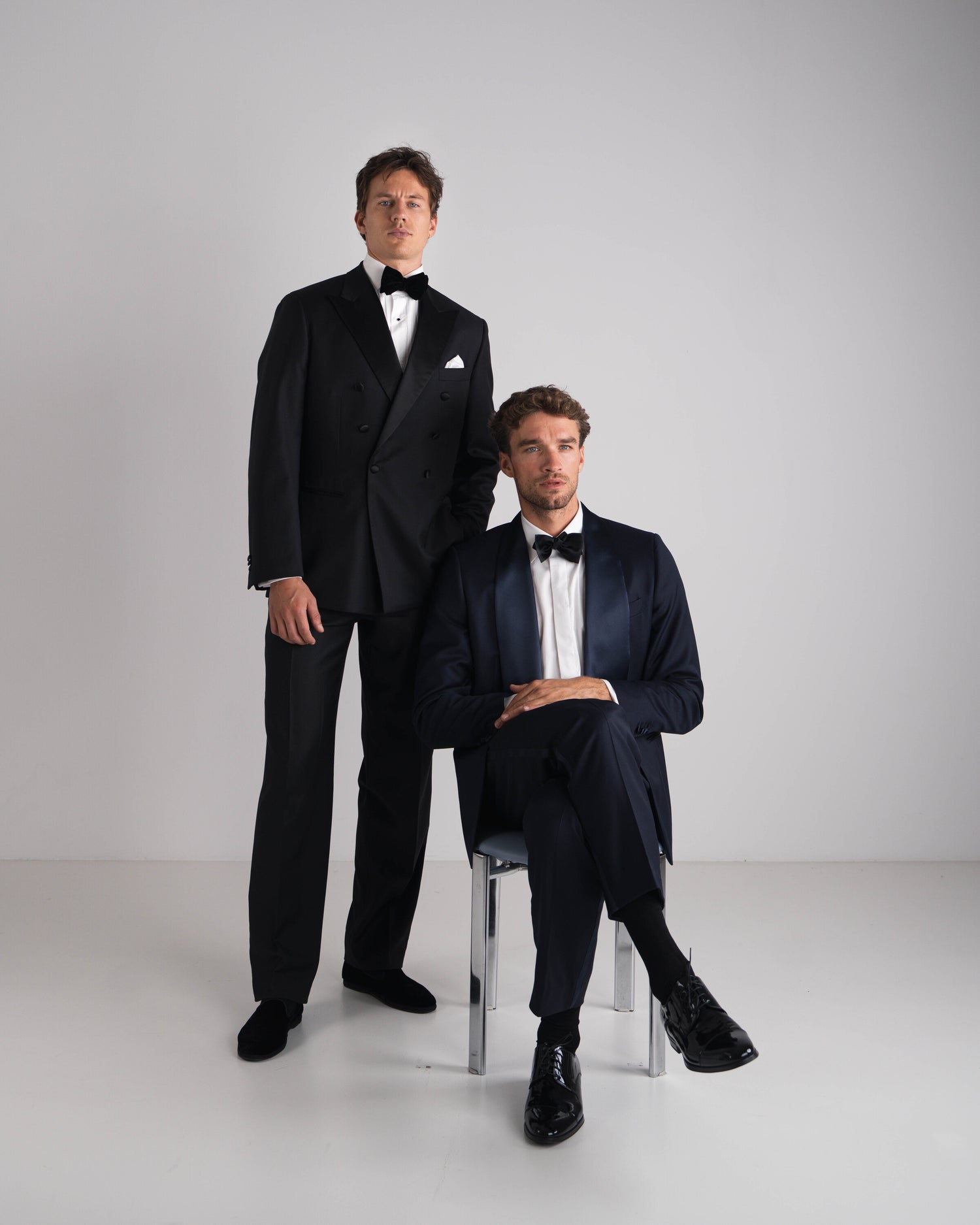 twee mannen naast elkaar in black tie kostuum de ene blauw en andere zwart double breasted