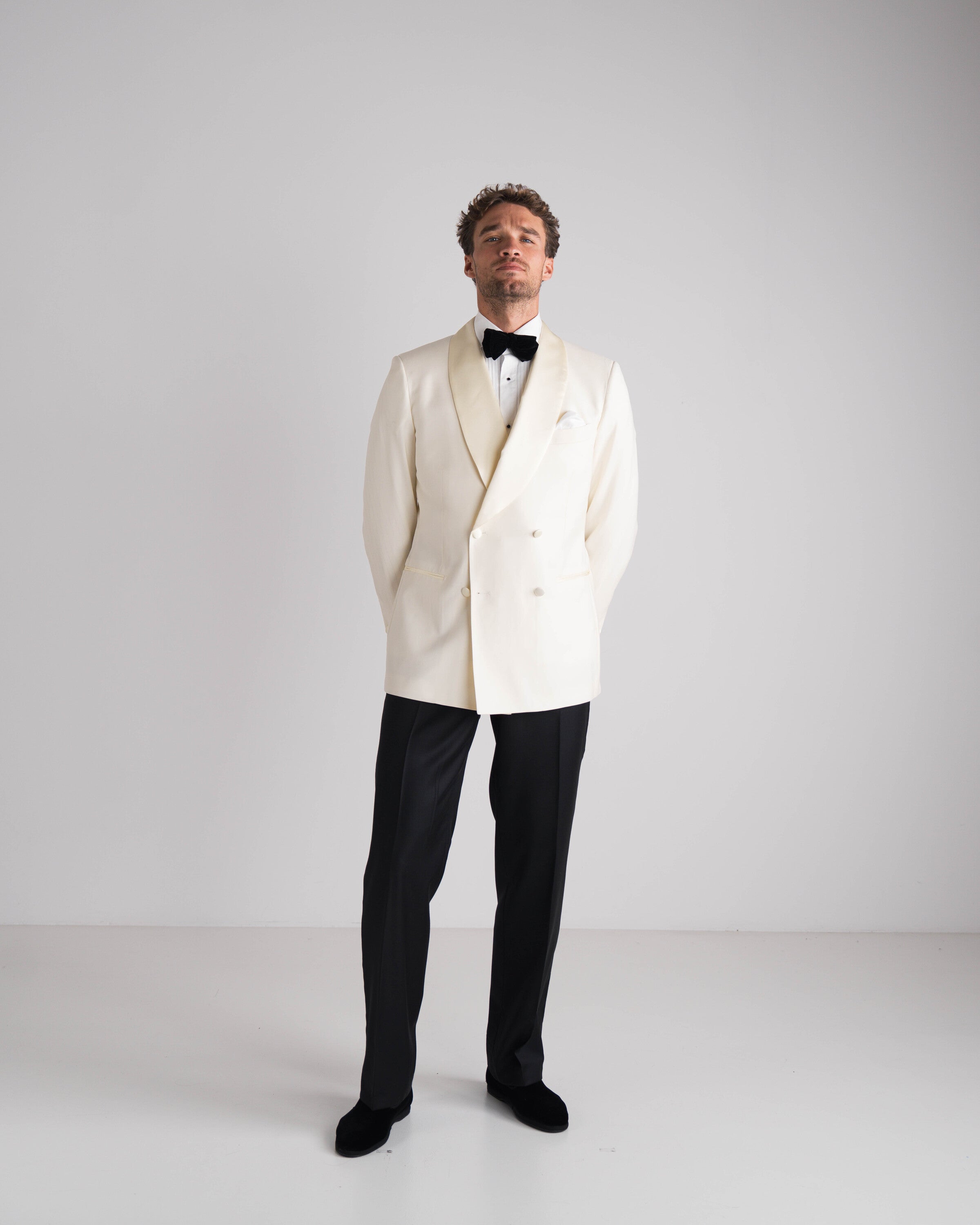 staande man in ivory double breasted jas enz zwarte strik en zwarte broek