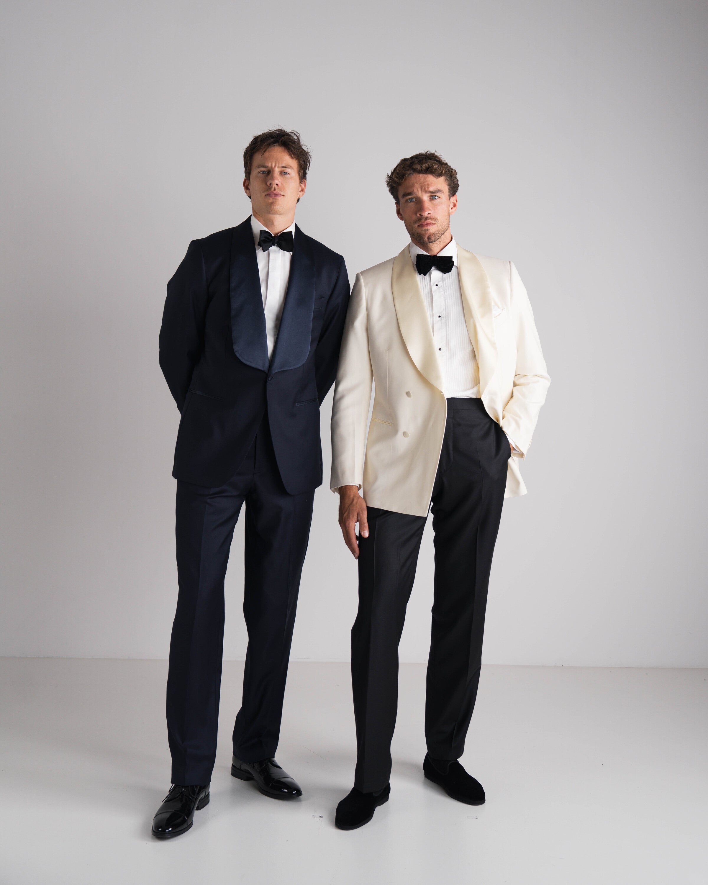 twee mannen naast elkaar in black tie kostuum de ene blauw en andere ivory double breasted