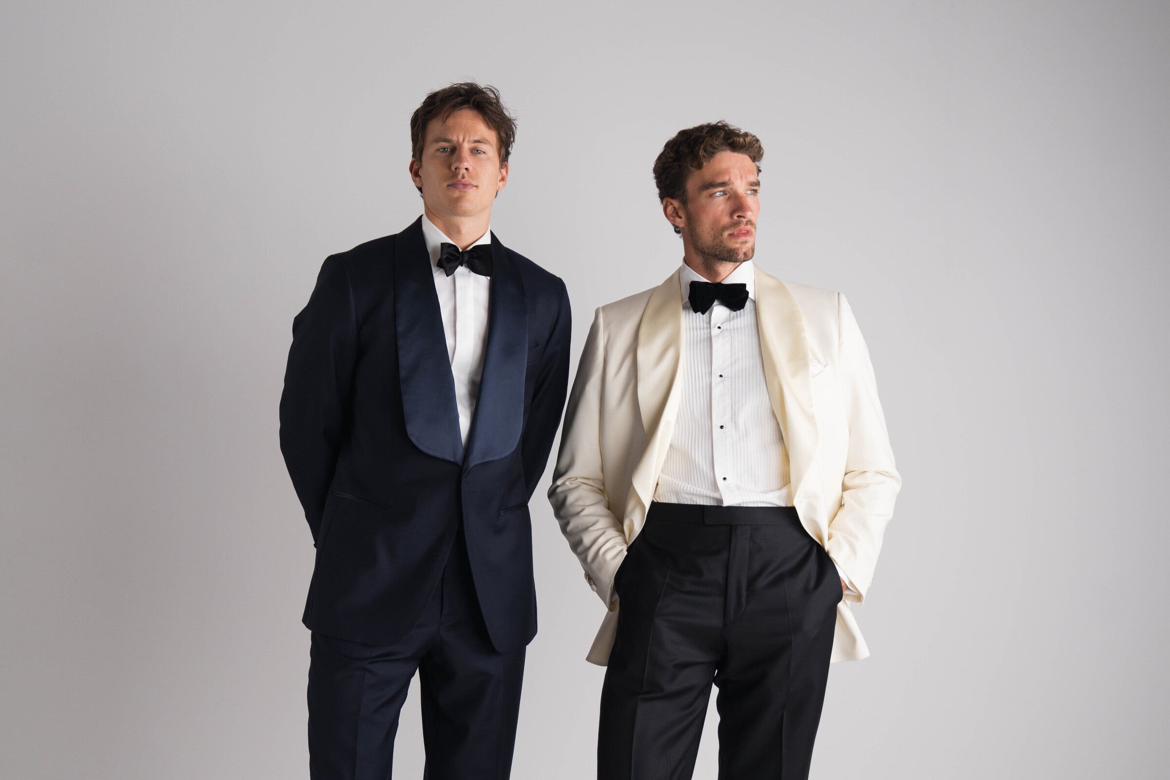 twee mannen naast elkaar in black tie kostuum de ene blauw en andere ivory double breasted