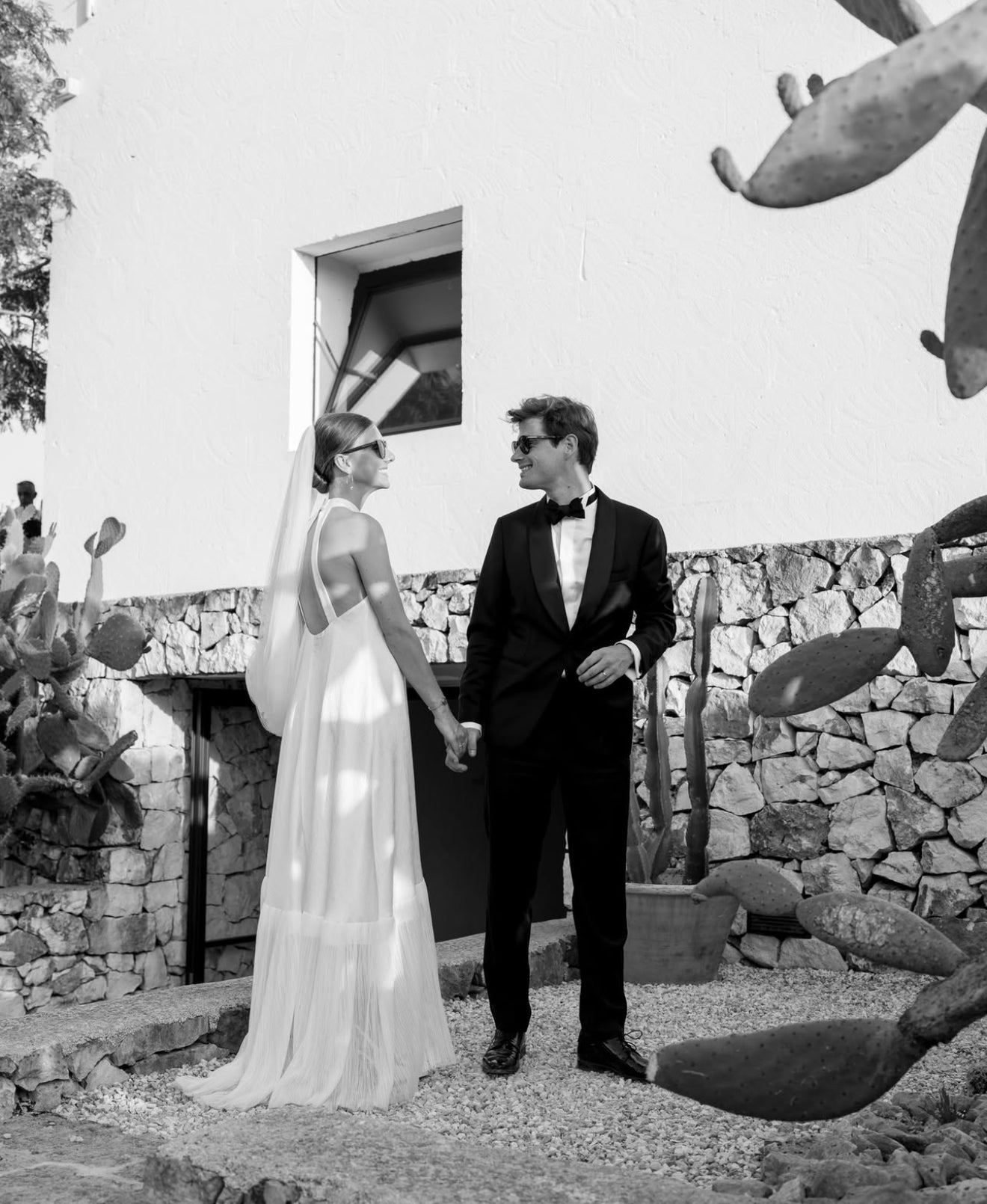 Man and woman in formal attire standing in front of a stone wall with cacti.