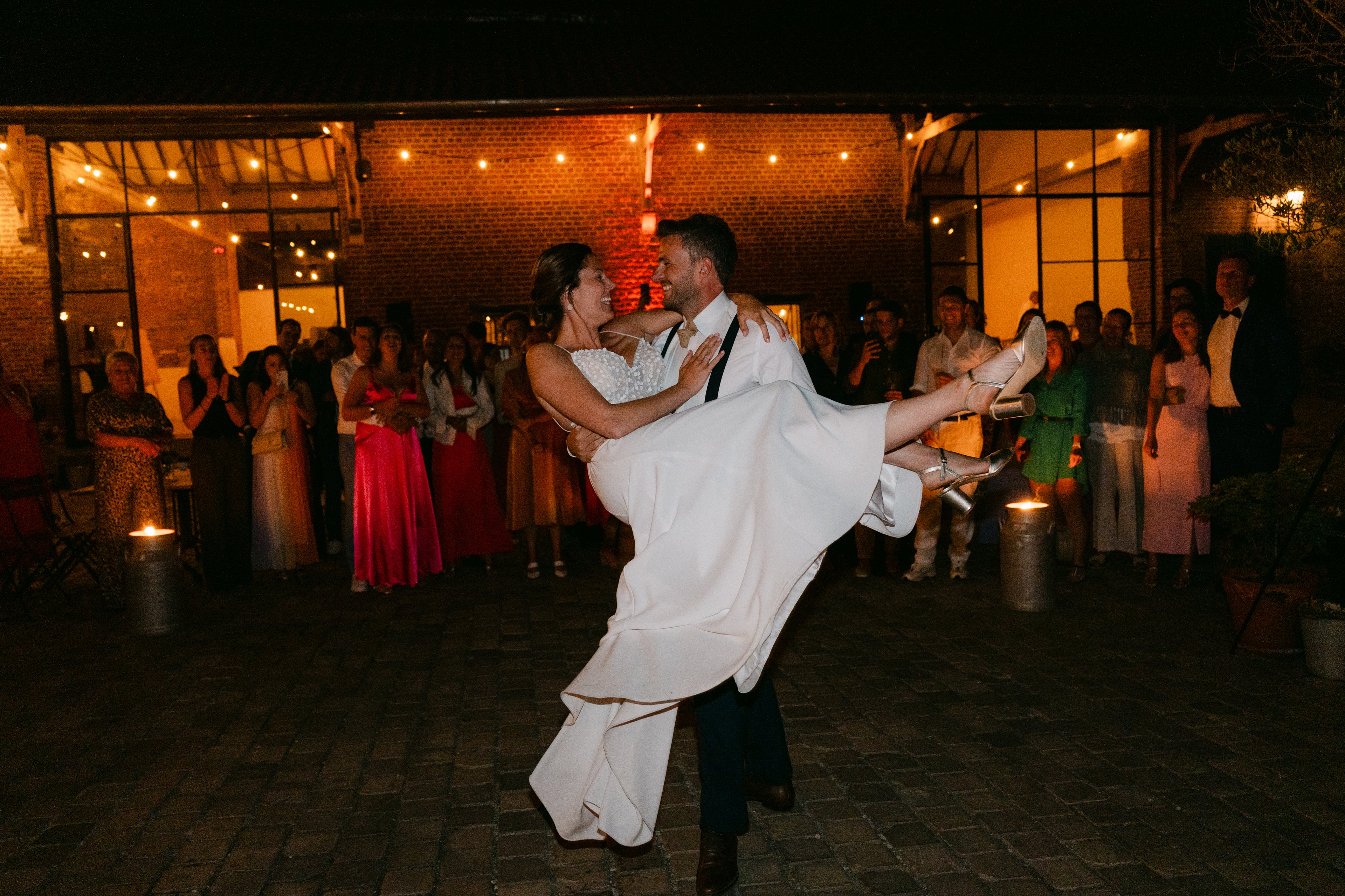 Groom lifting bride at a wedding reception with guests in the background.