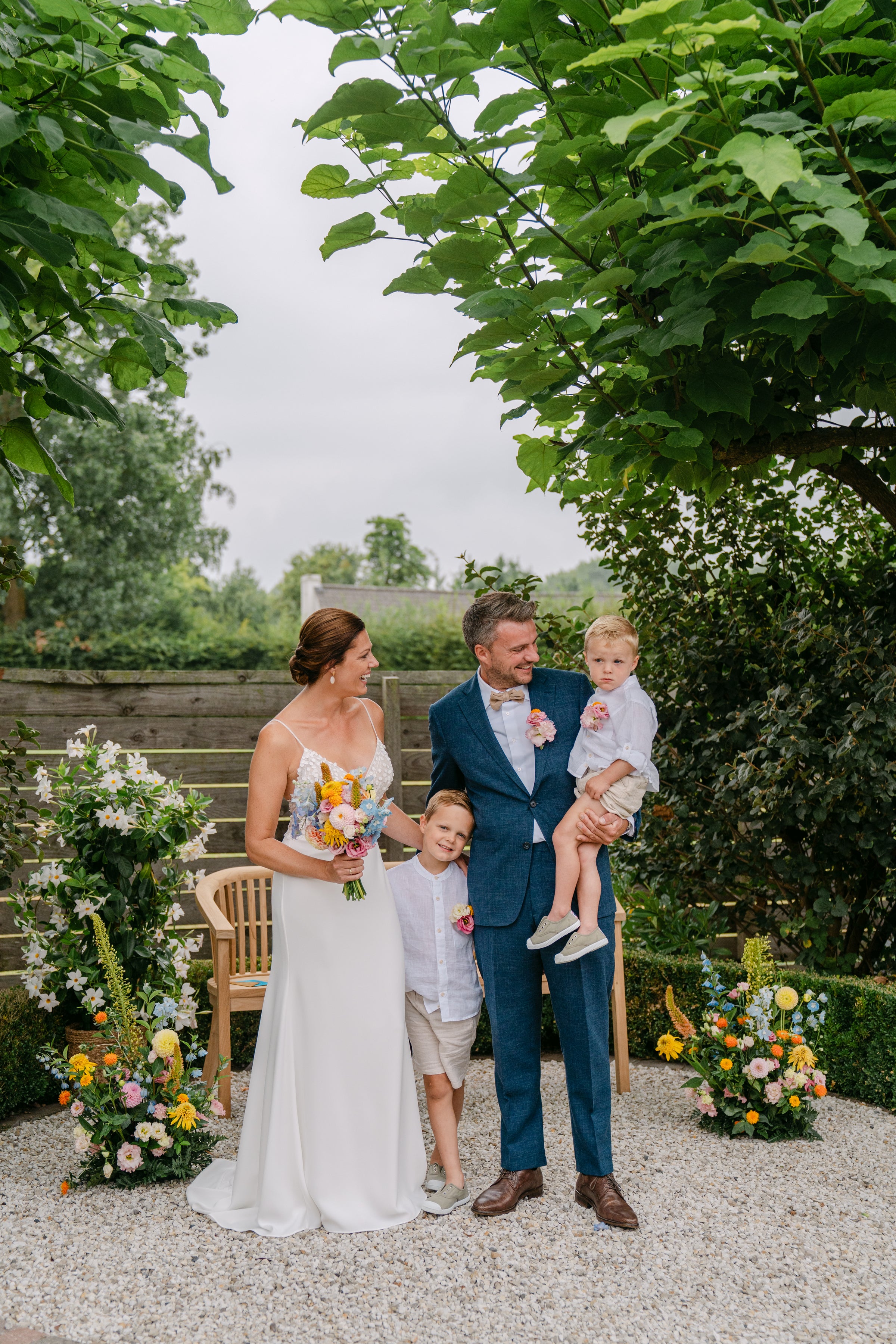 Wedding couple with two children standing outdoors in a garden setting.