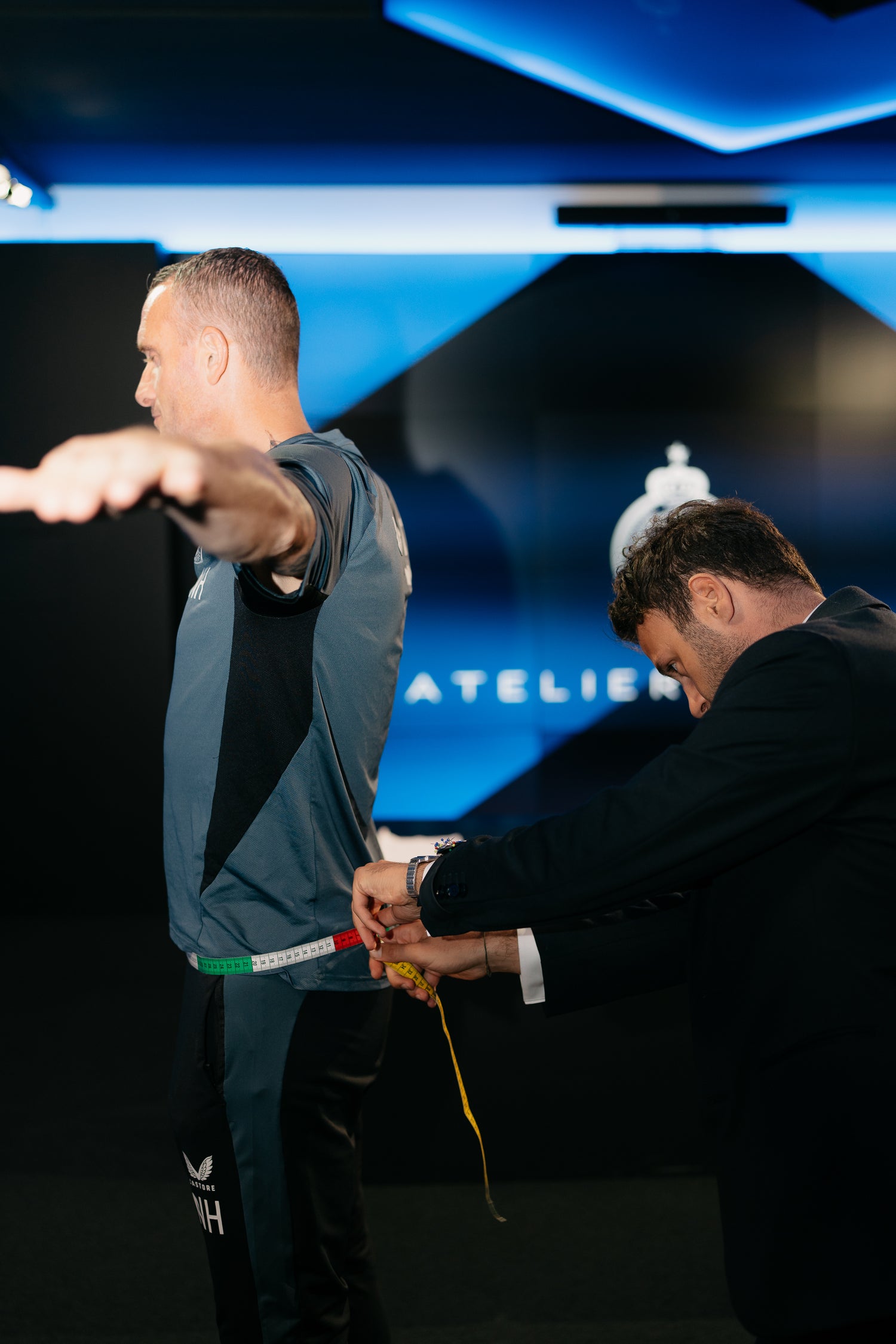 Nicky Hayen van Club Brugge wordt opgemeten voor een maatpak bij Atelier ACÀN, blauwe muur met logo op de achtergrond