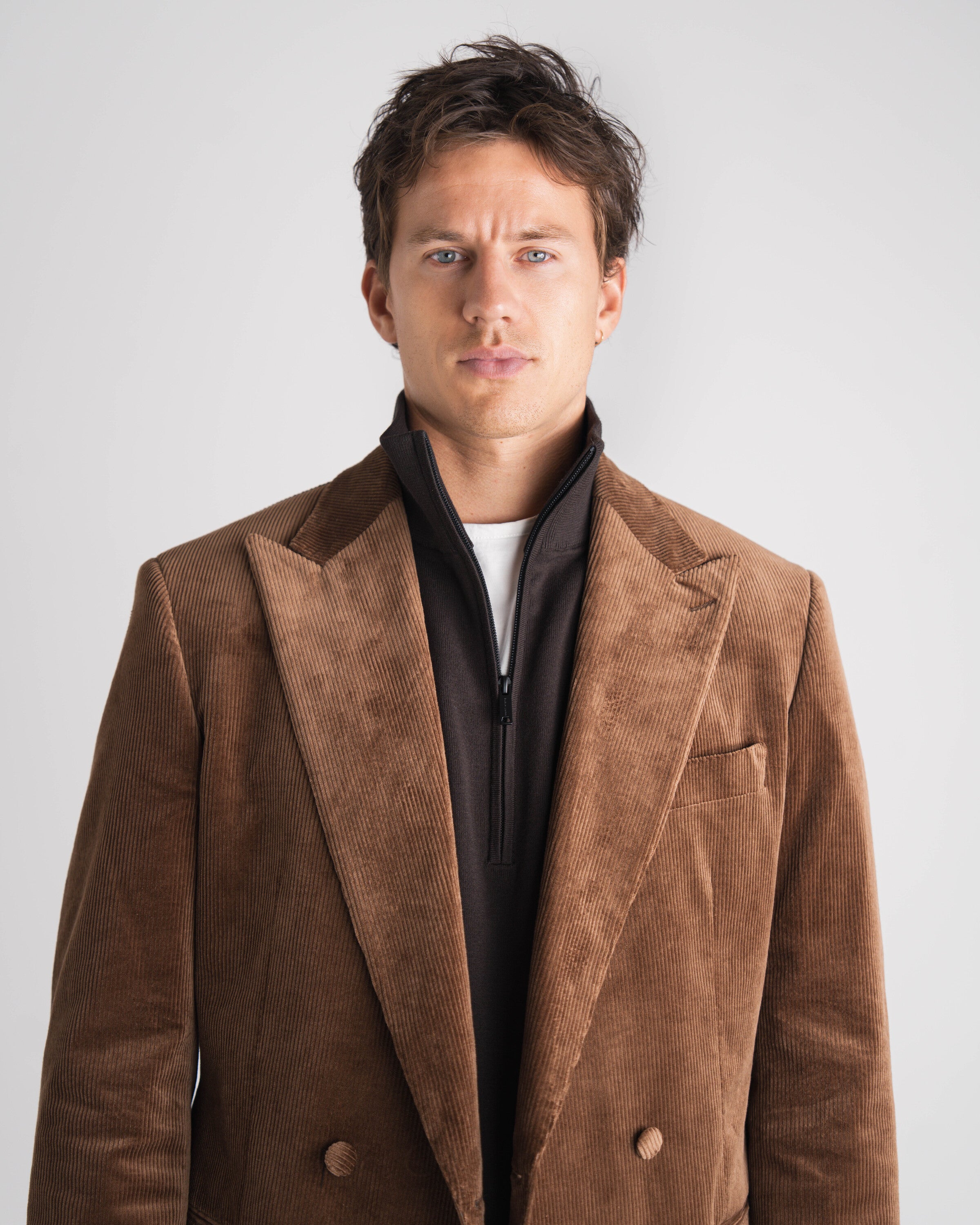 Man in een bruin ribfluwelen pak op maat tegen een neutrale achtergrond