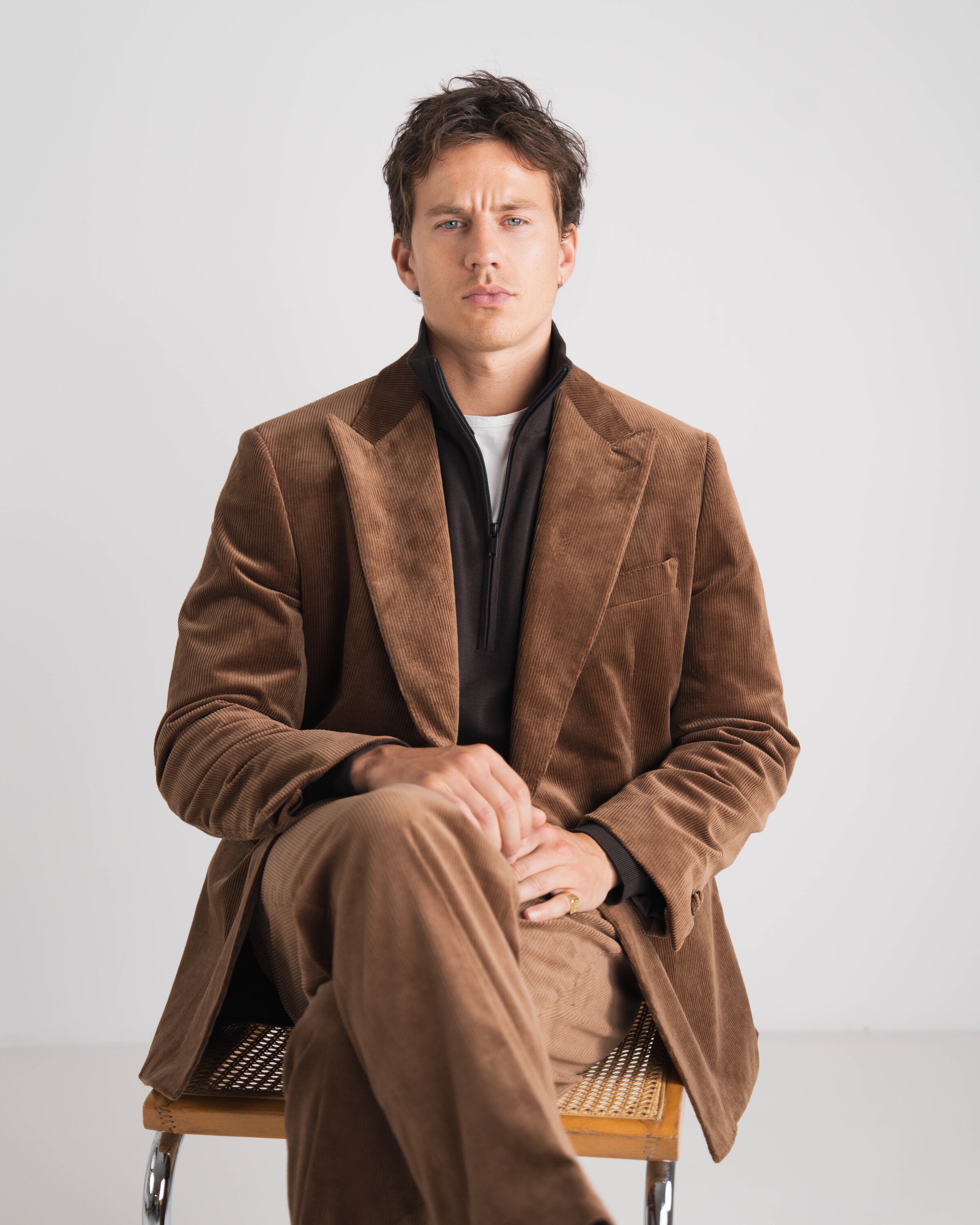 donkerbruin ribfluweel kostuum zittende man met bruine trui