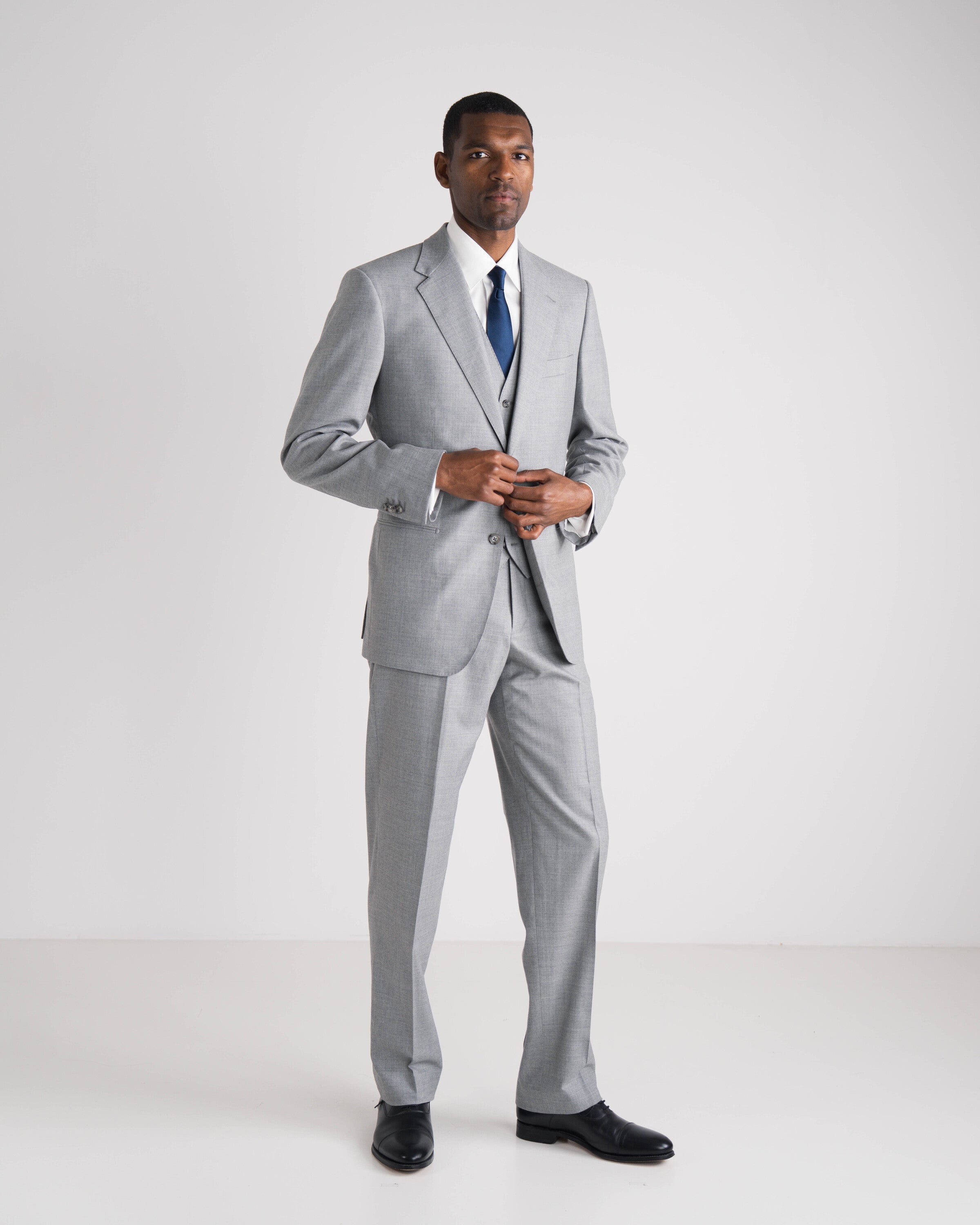 man in drie delig lichtgrijs kostuum met blauwe das