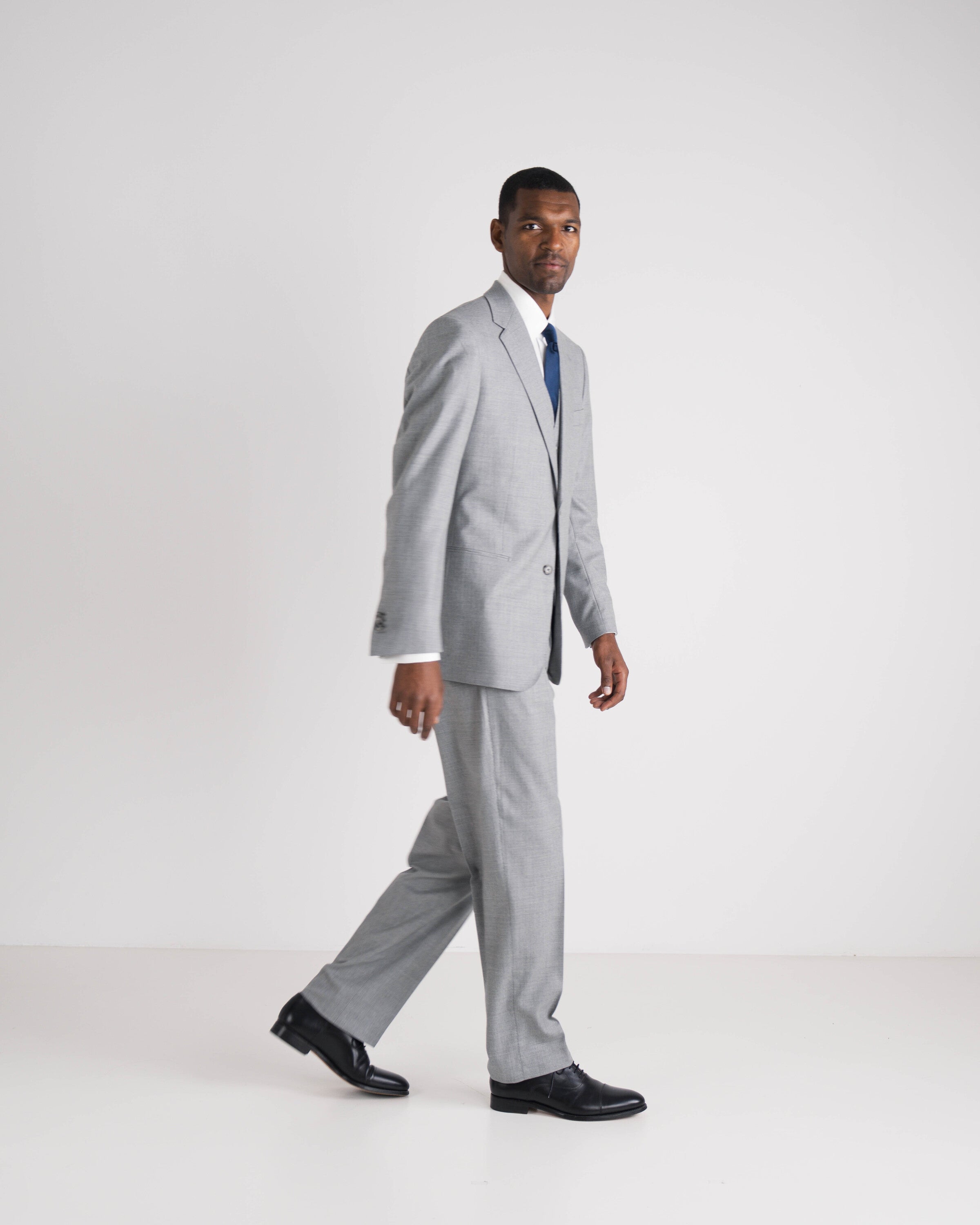 man in drie delig lichtgrijs kostuum met blauwe das