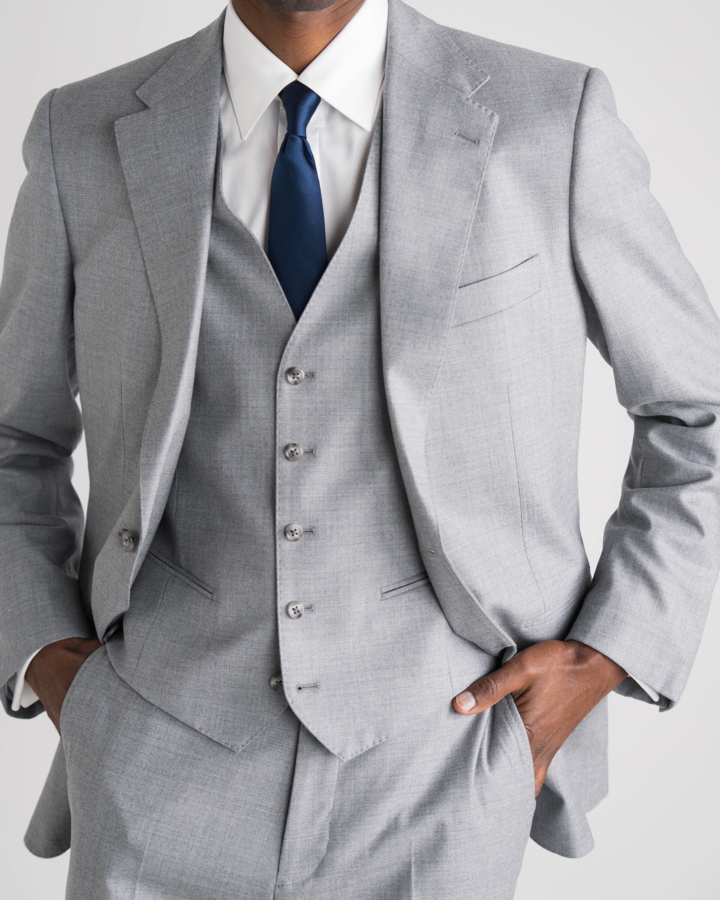 man in drie delig lichtgrijs kostuum met blauwe das