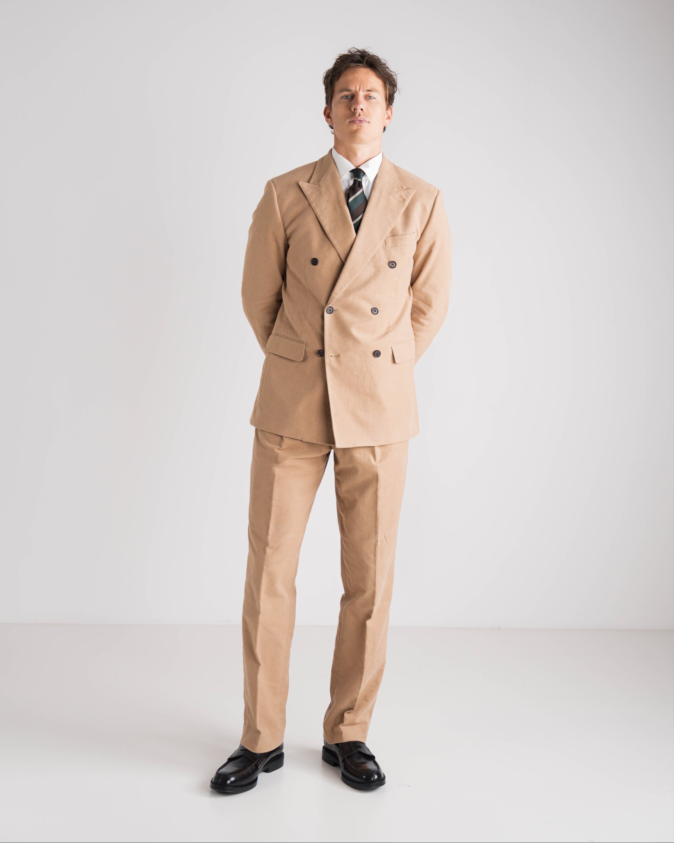 Man wearing a beige suit with a white shirt and black shoes on a white background