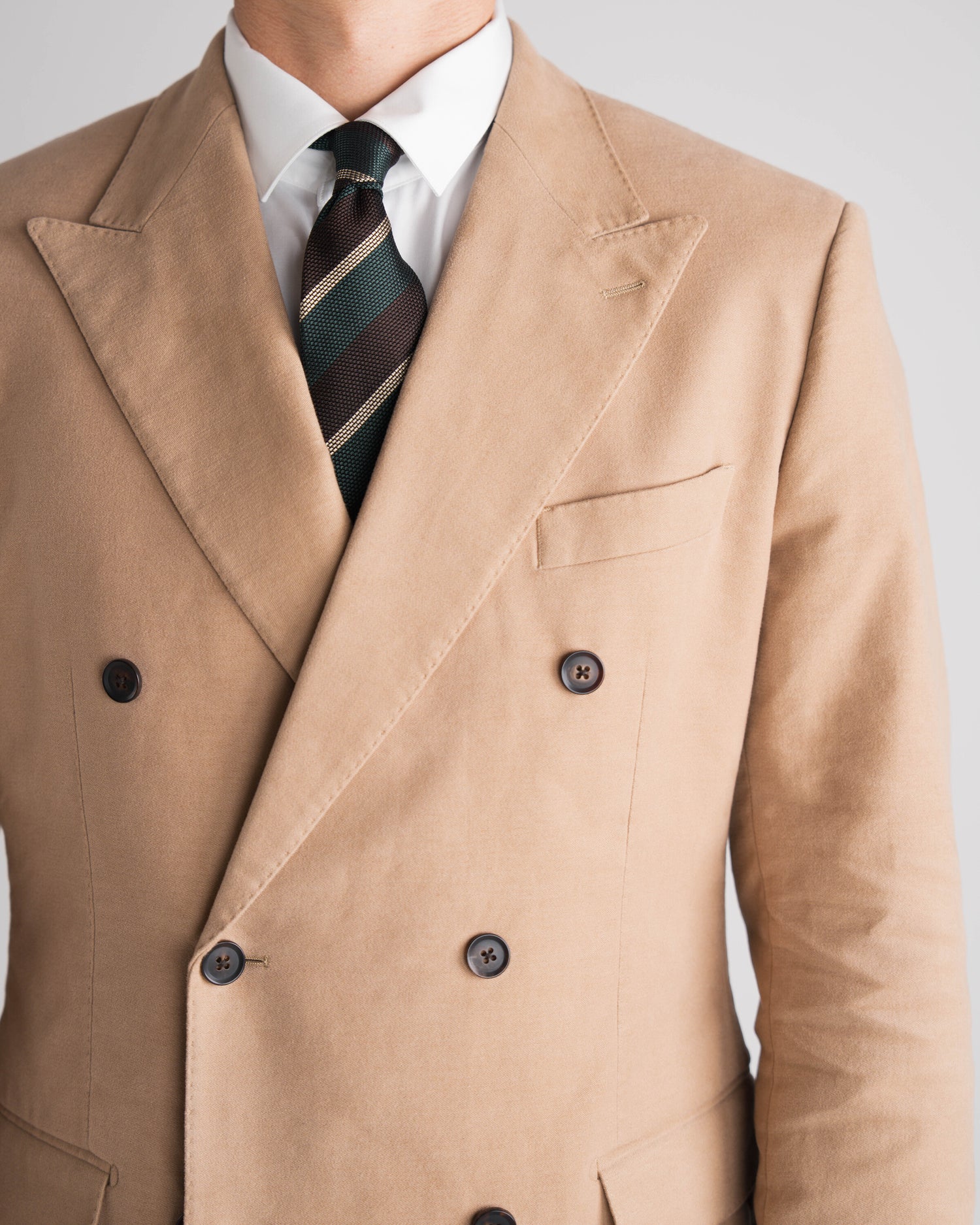 Tan double-breasted coat with a white shirt and striped tie on a light gray background