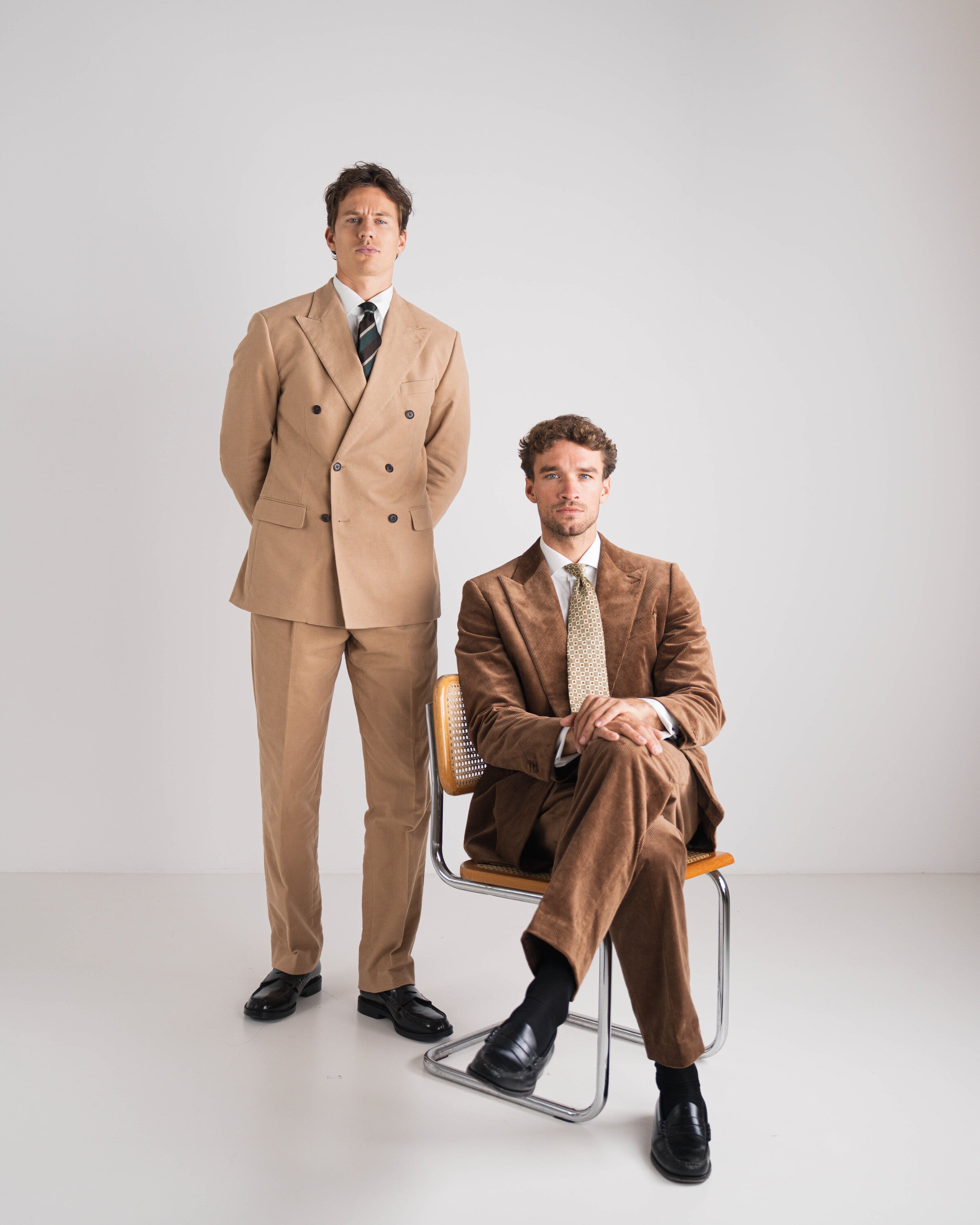 twee mannen in bruin corduroy kostuum en andere in camel double breasted en das 