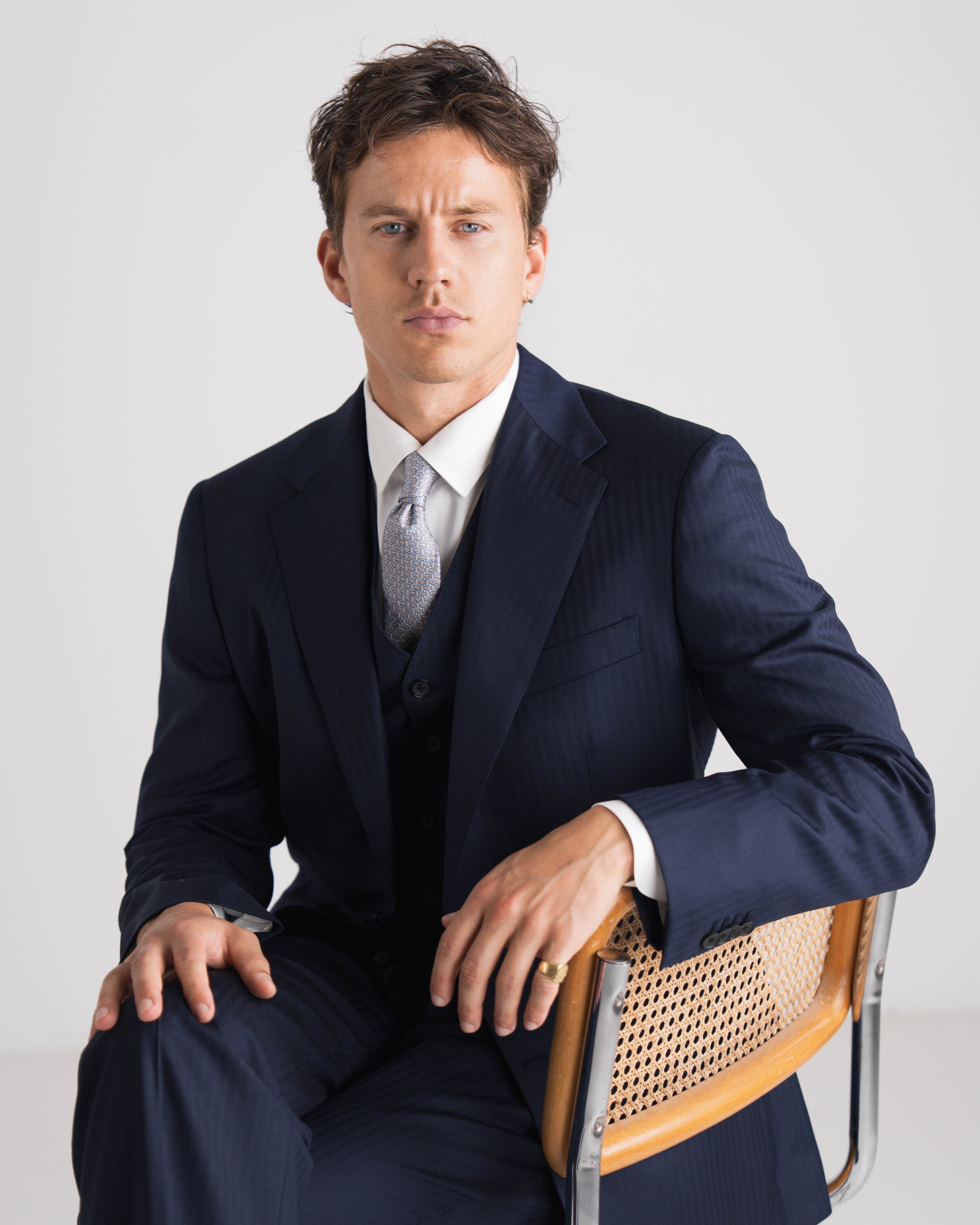 driedelig donker blauw wit hemd en grijze das al zittend