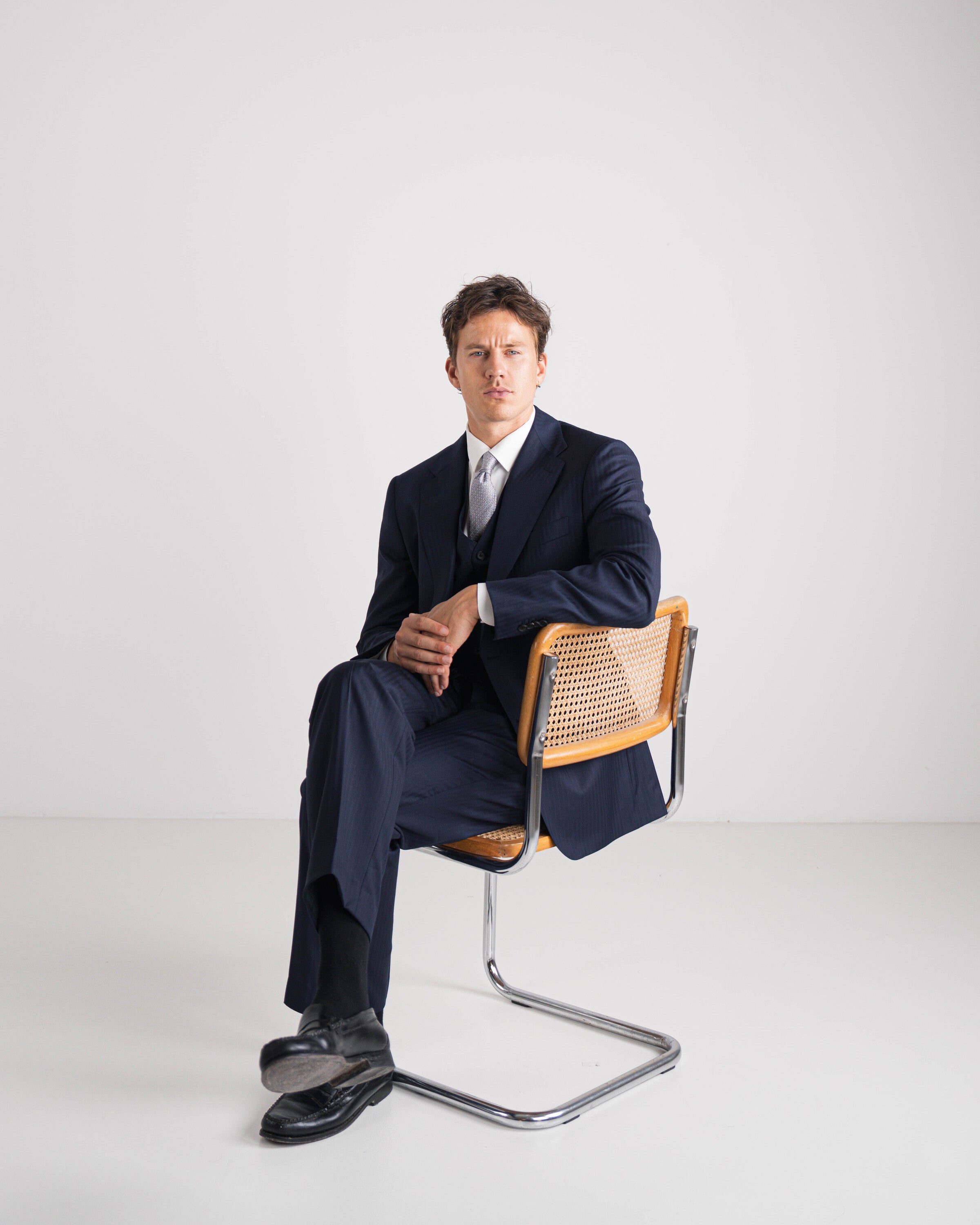 driedelig donker blauw wit hemd en grijze das al zittend