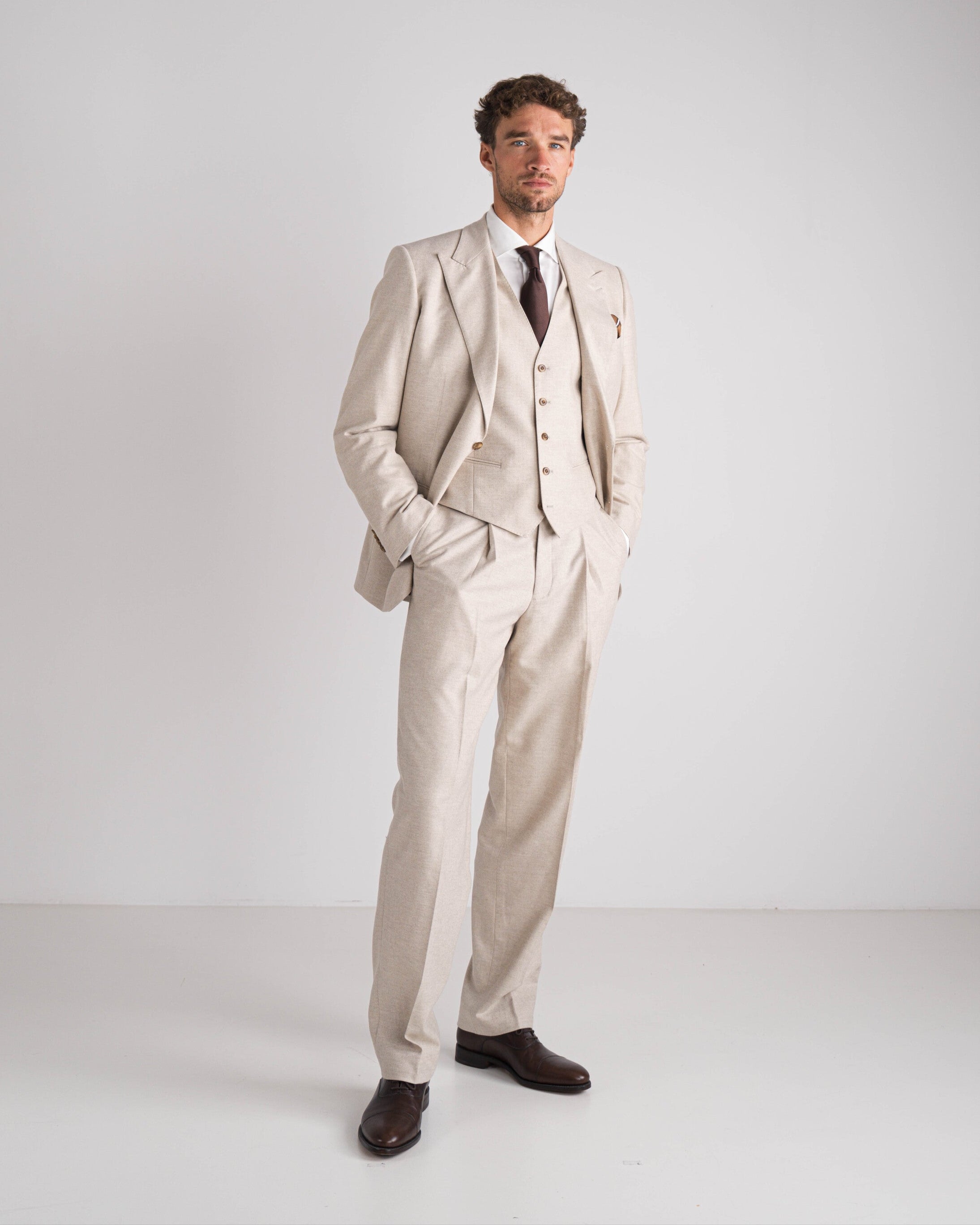 Man wearing a beige suit with a white shirt and dark tie on a white background