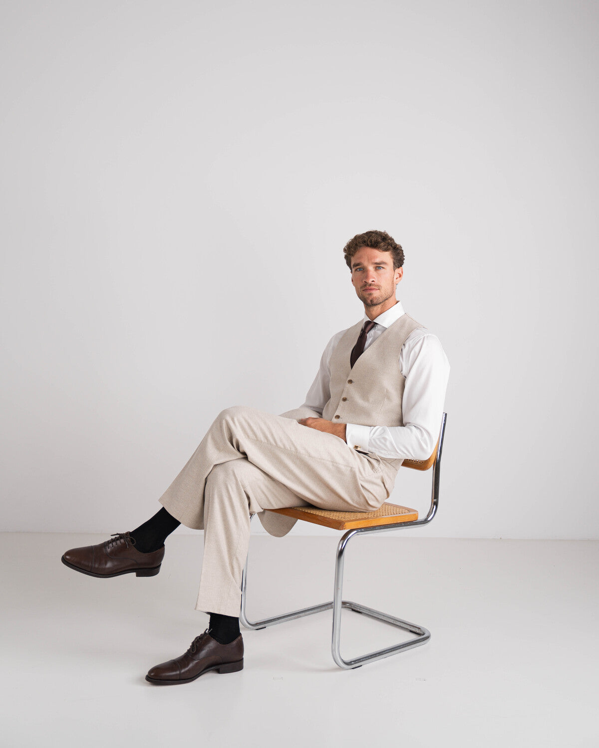 man in driedelig beige kostuum met wit hemd en bruine das