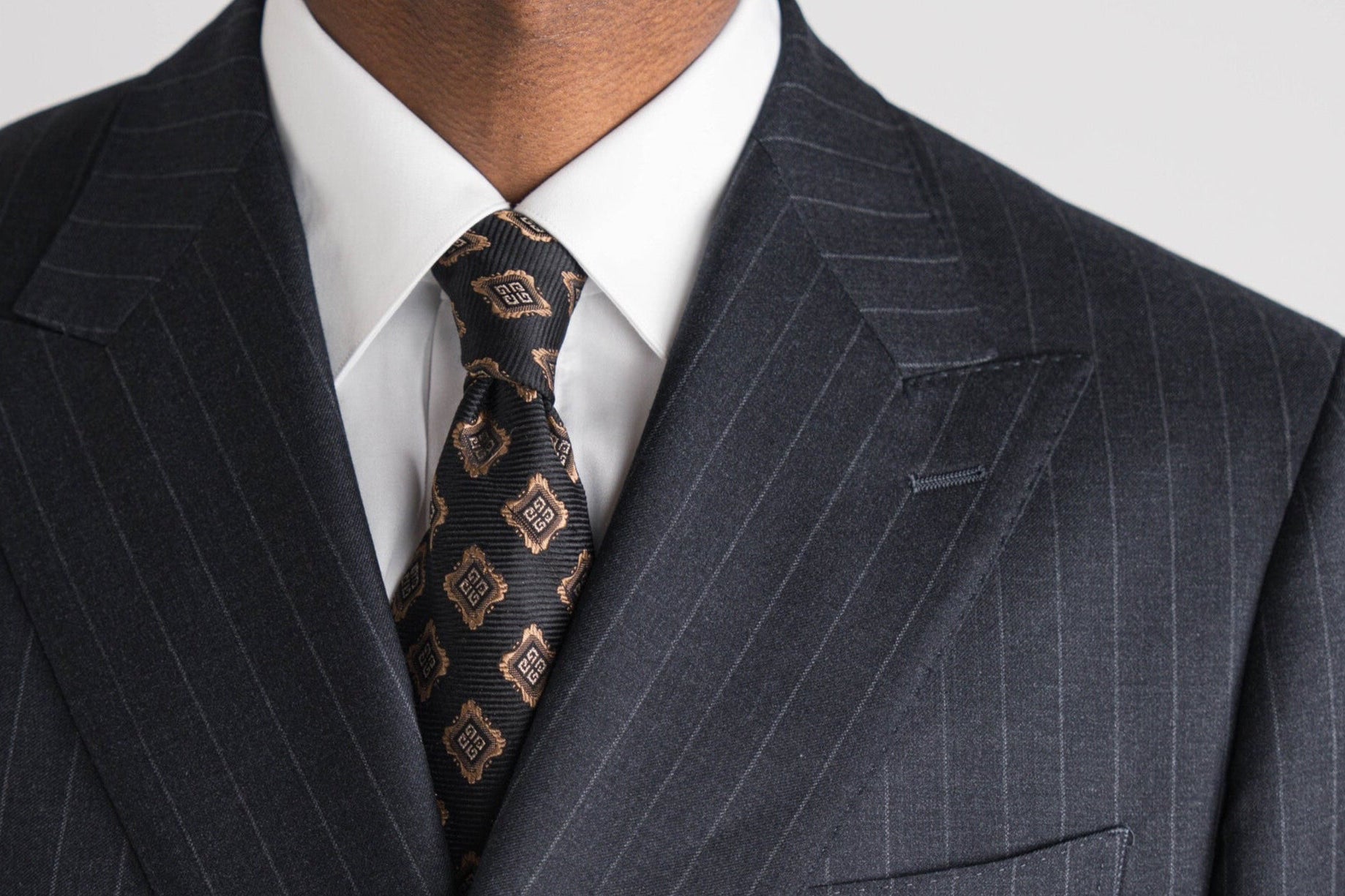 Man in donker krijtstreep pak met wit overhemd en stropdas met patroon op een lichtgrijze achtergrond