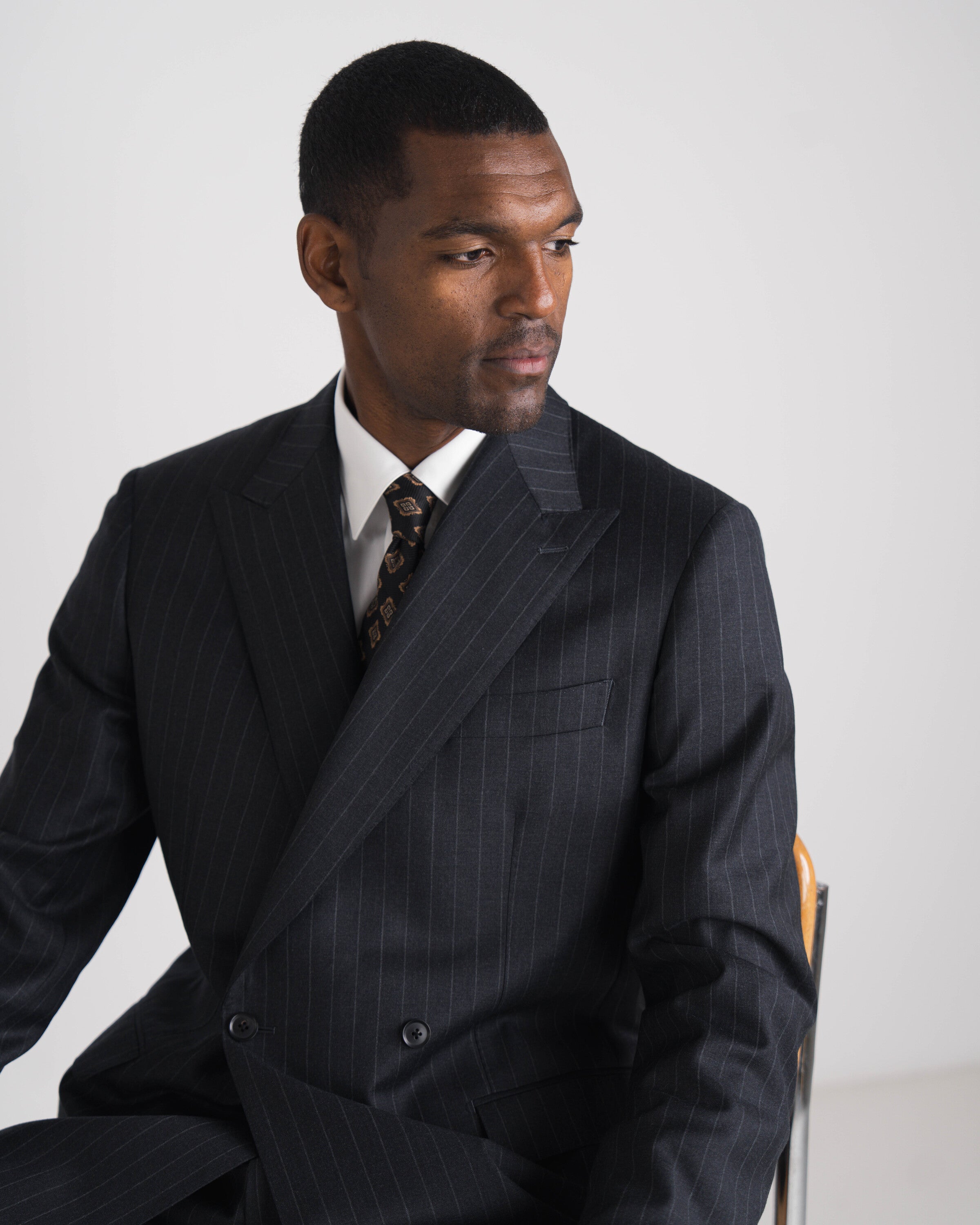 Man wearing a dark pinstripe suit and tie against a plain background