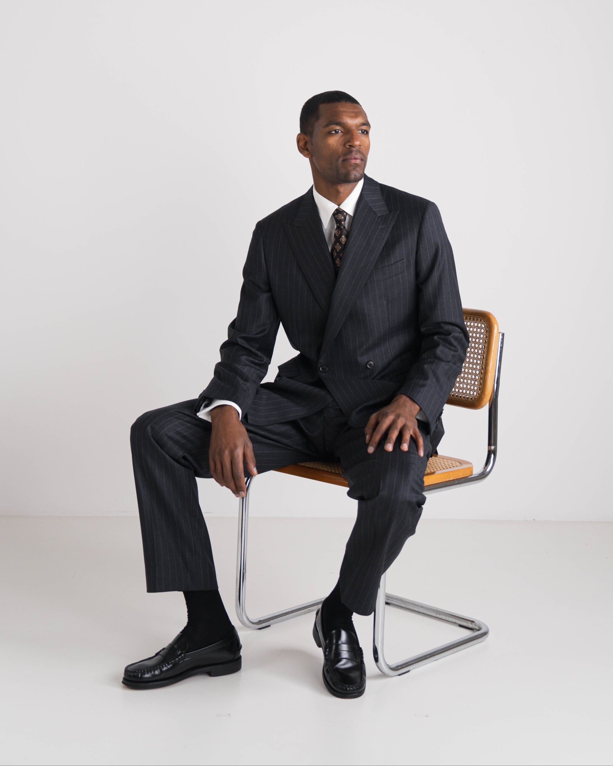 Man in a black pinstripe suit sitting on a chair against a white background