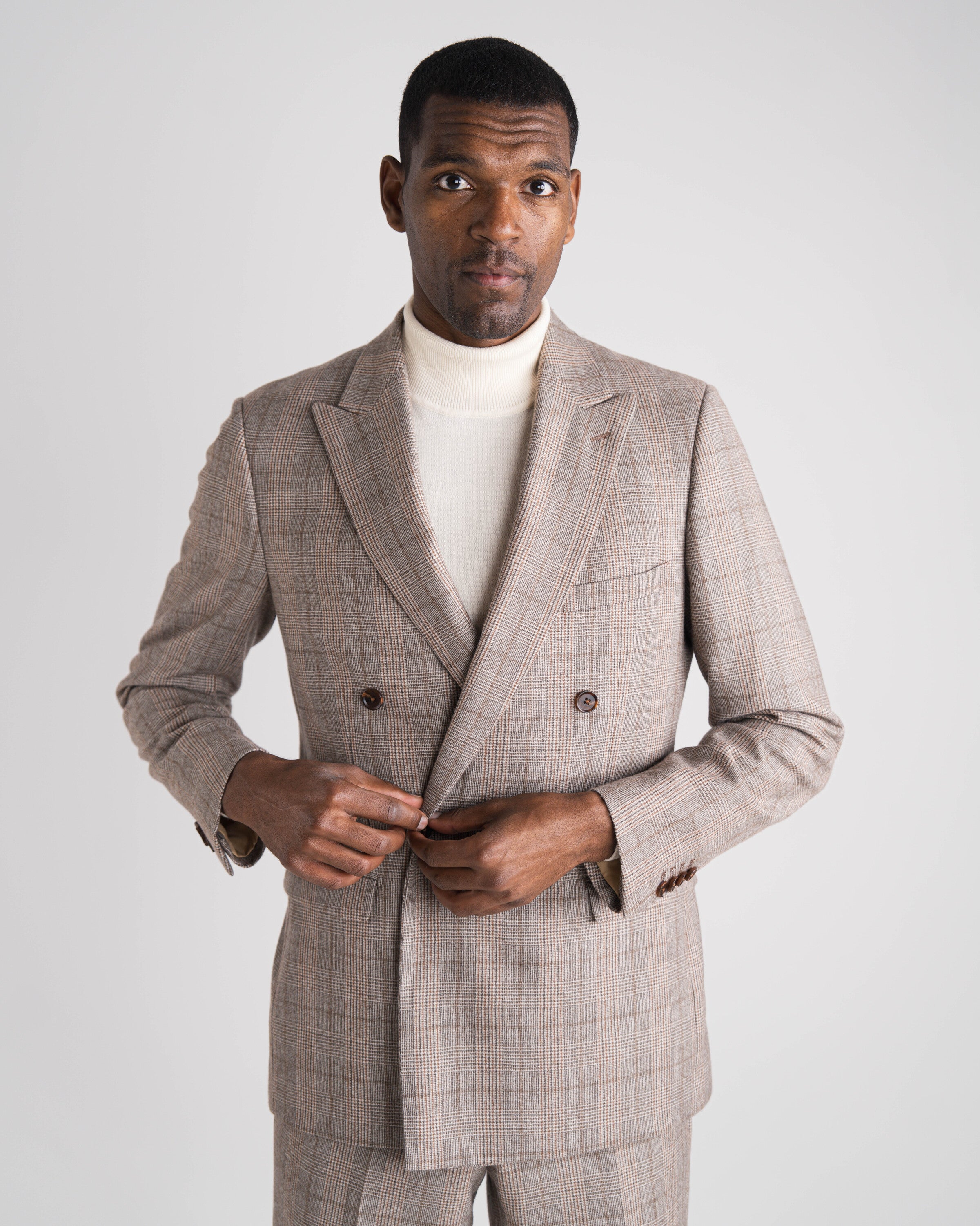 Man wearing a gray checkered suit with a white turtleneck against a plain background