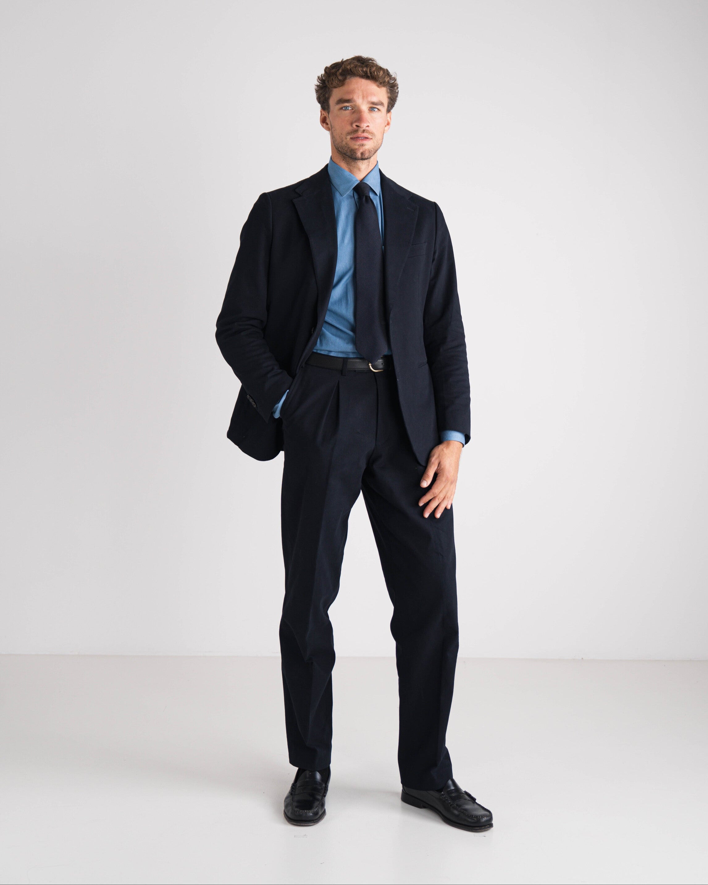 Man wearing a black suit with a blue shirt and tie on a white background