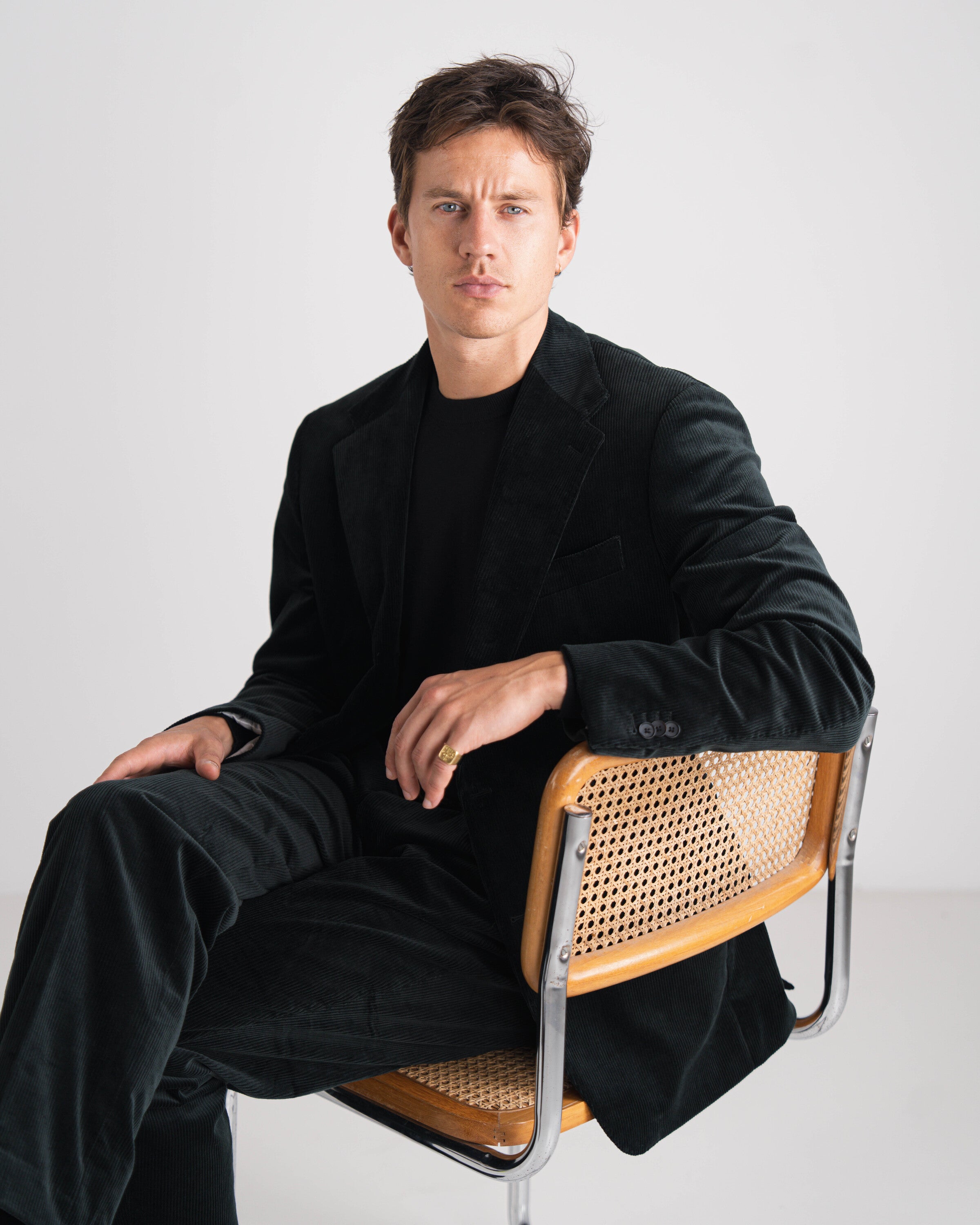 Man in a black coat sitting on a chair with a white background