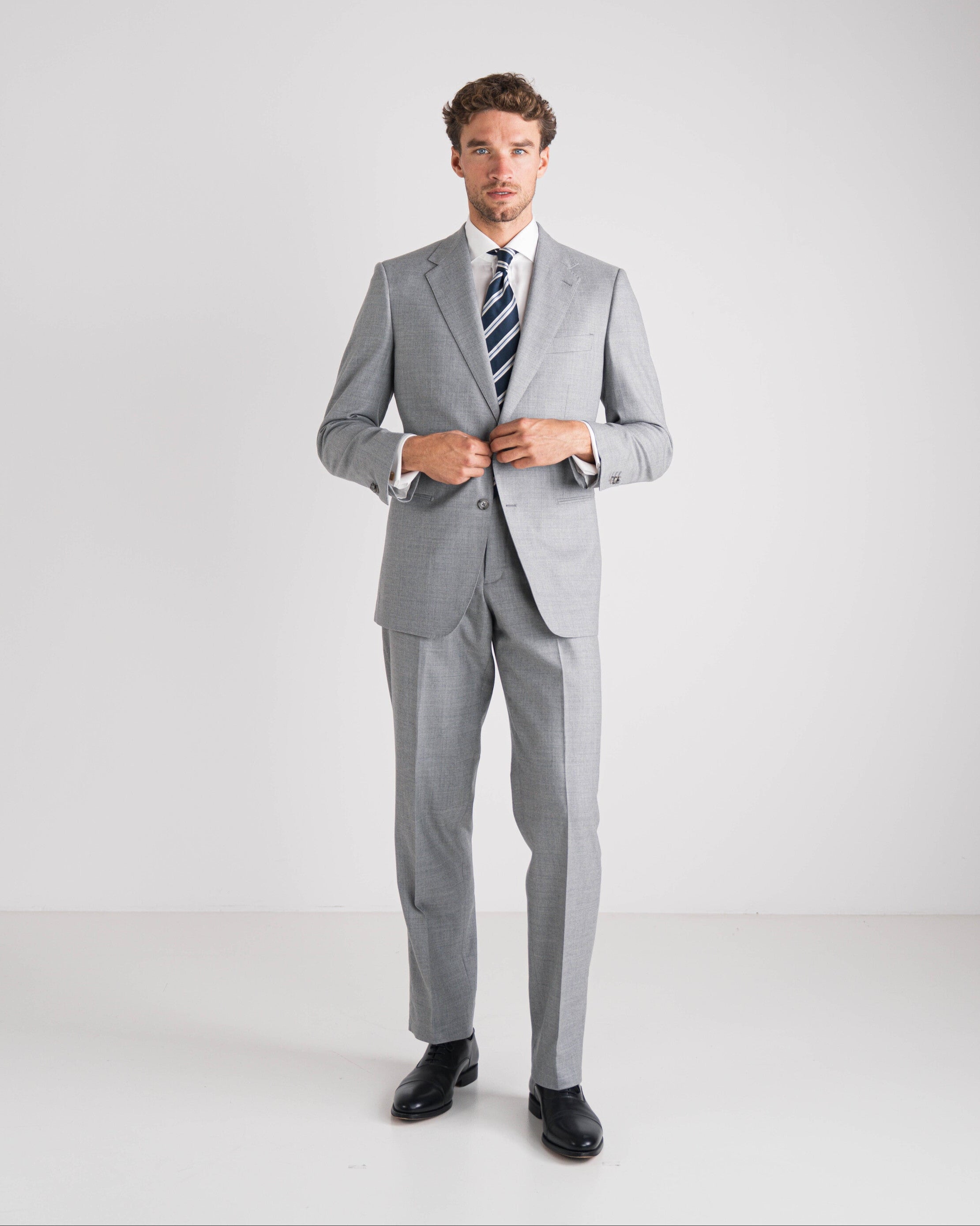 Man in grijs maatpak met wit overhemd en gestreepte das op een witte achtergrond