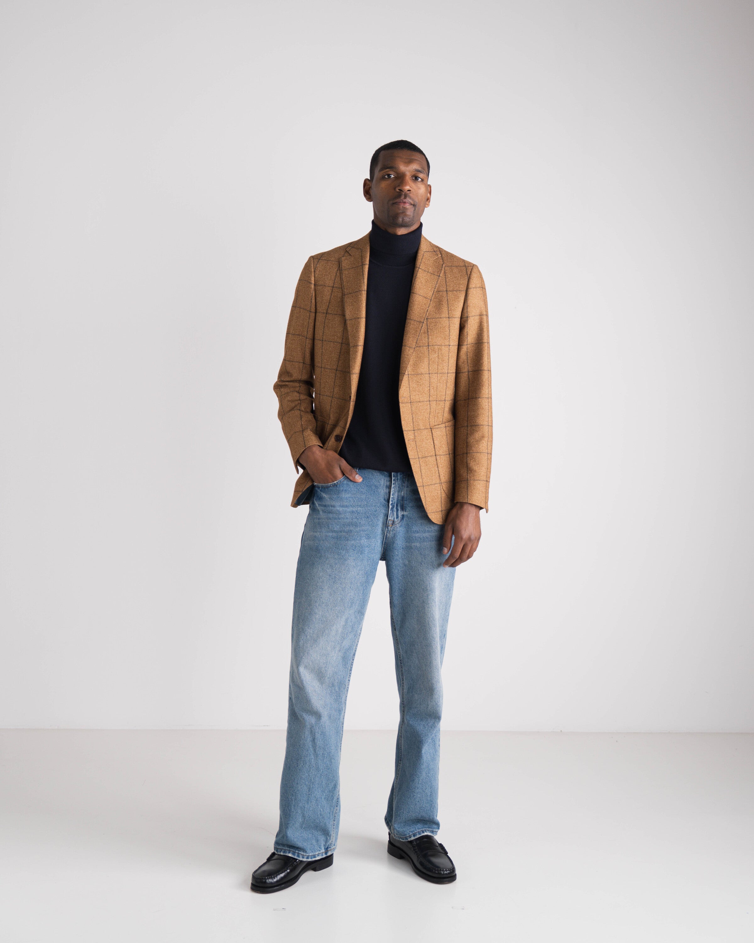 man met jeans en blauwe koltrui met bruin geruit blazer