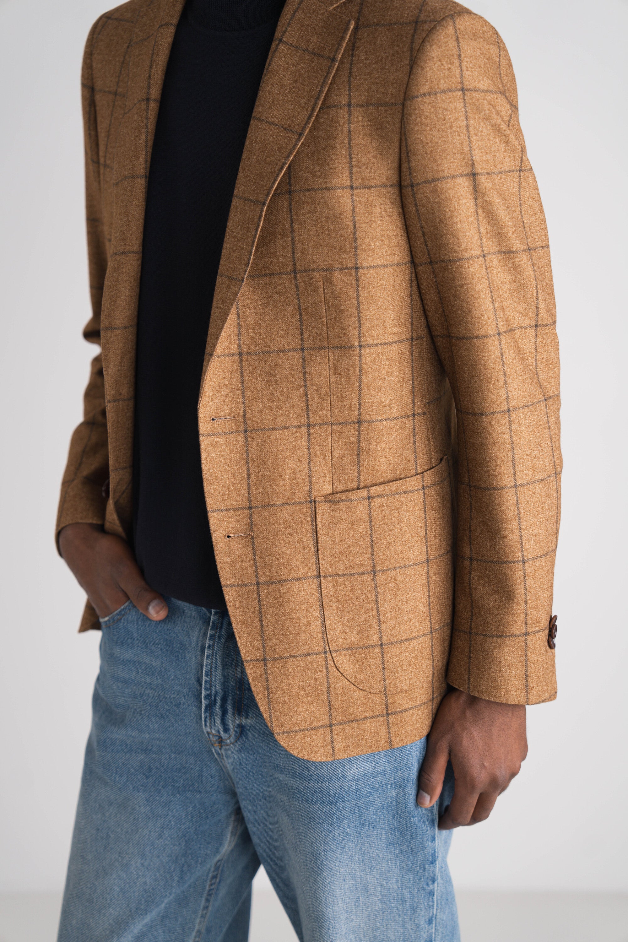 man met jeans en blauwe koltrui met bruin geruit blazer
