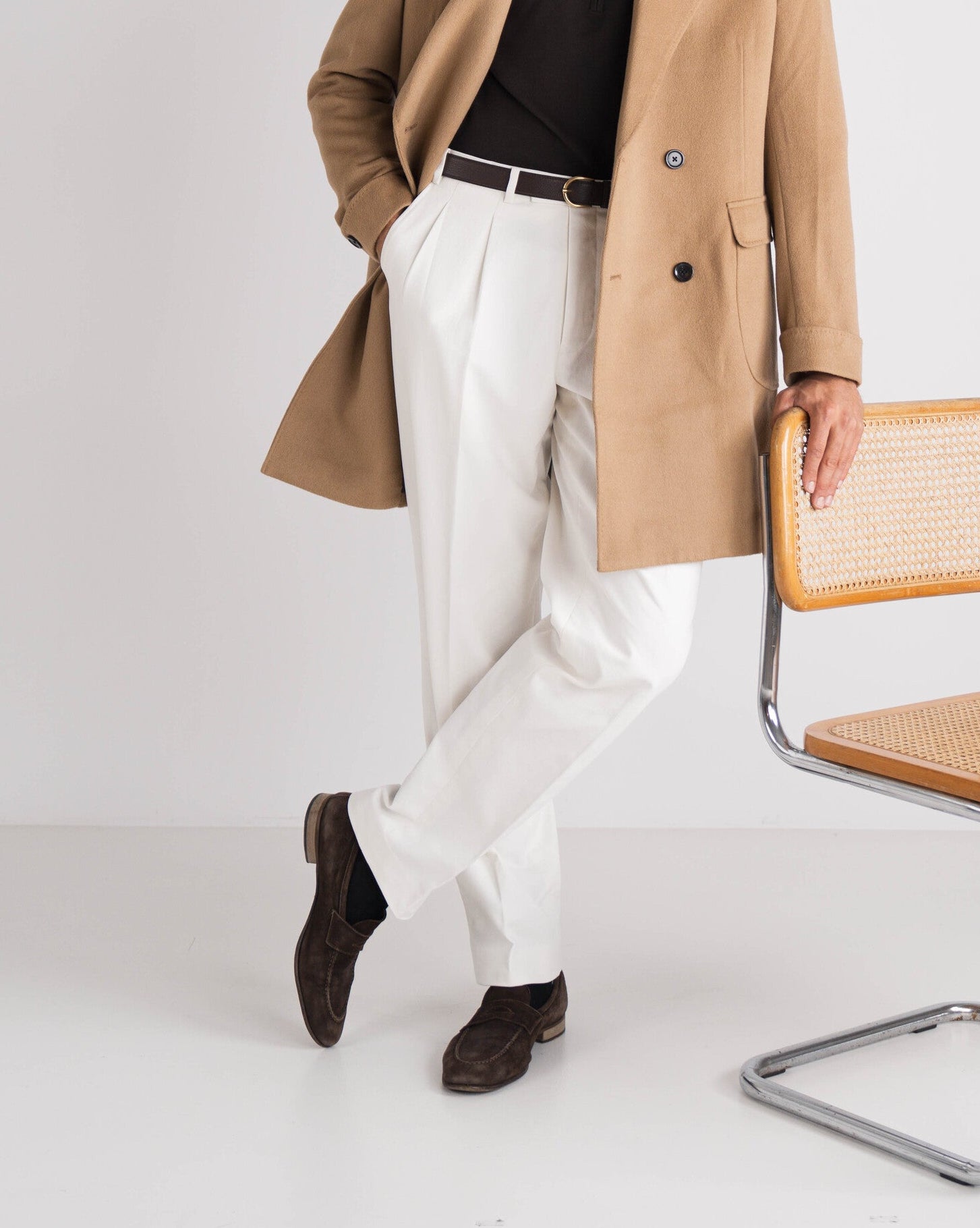 man met bruine trui en camel overcoat en witte broek