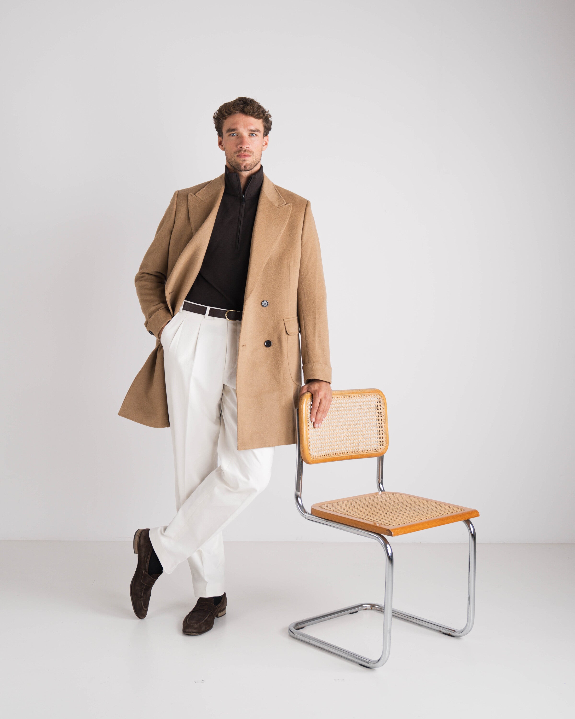 man met bruine trui en camel overcoat en witte broek