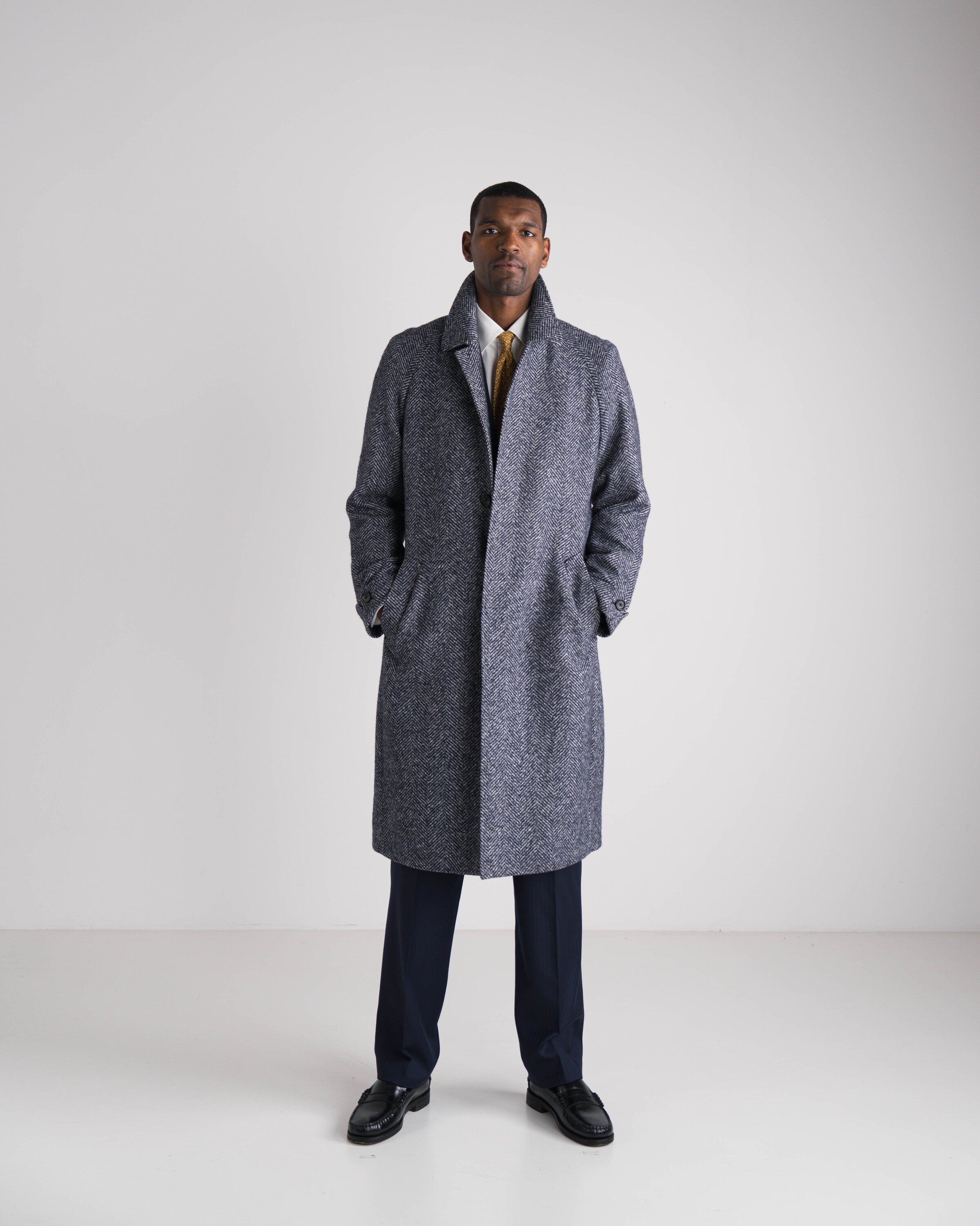 man in grijze mantel met blauw kostuum en gele das