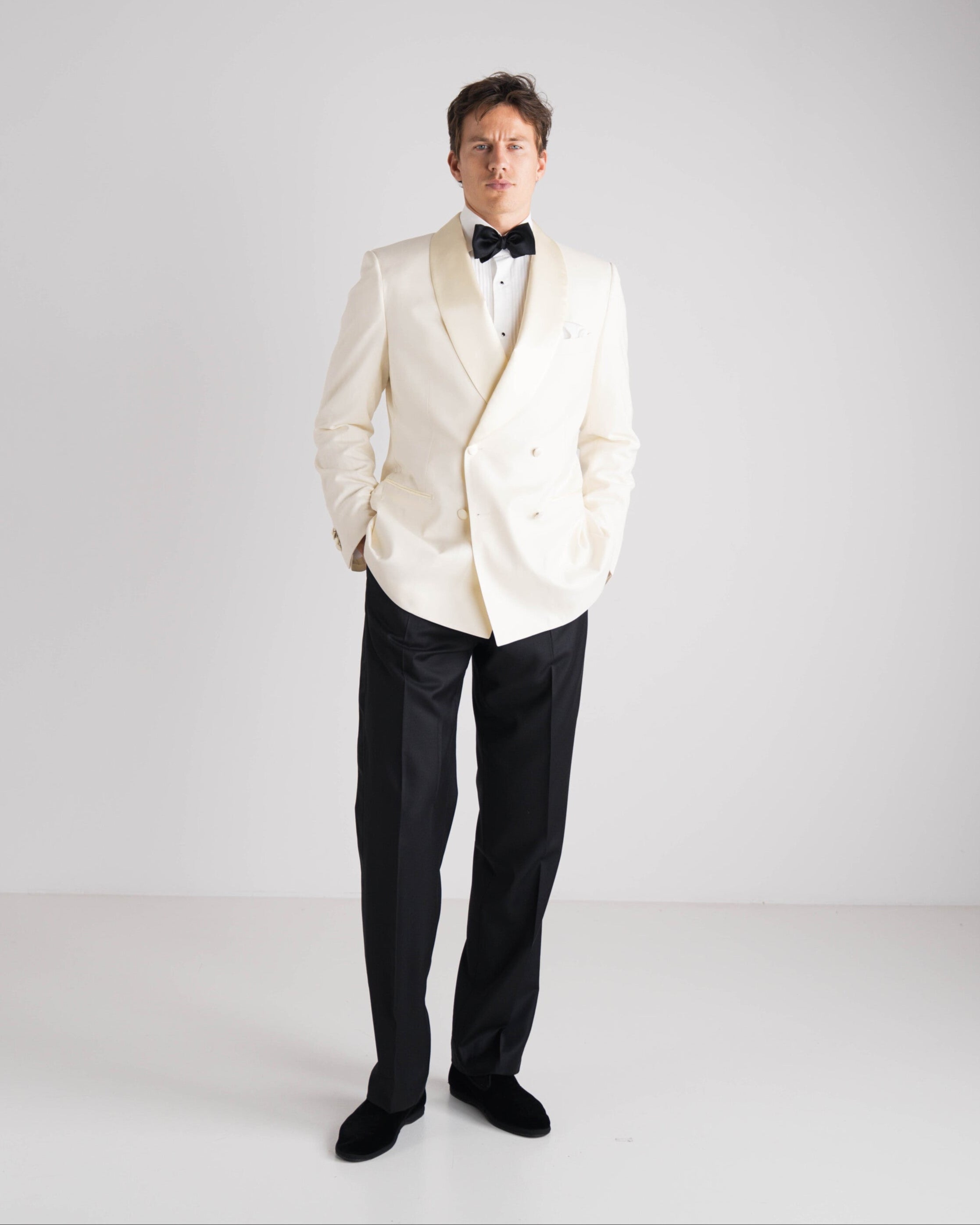 Man wearing a white tuxedo with black bow tie on a plain background