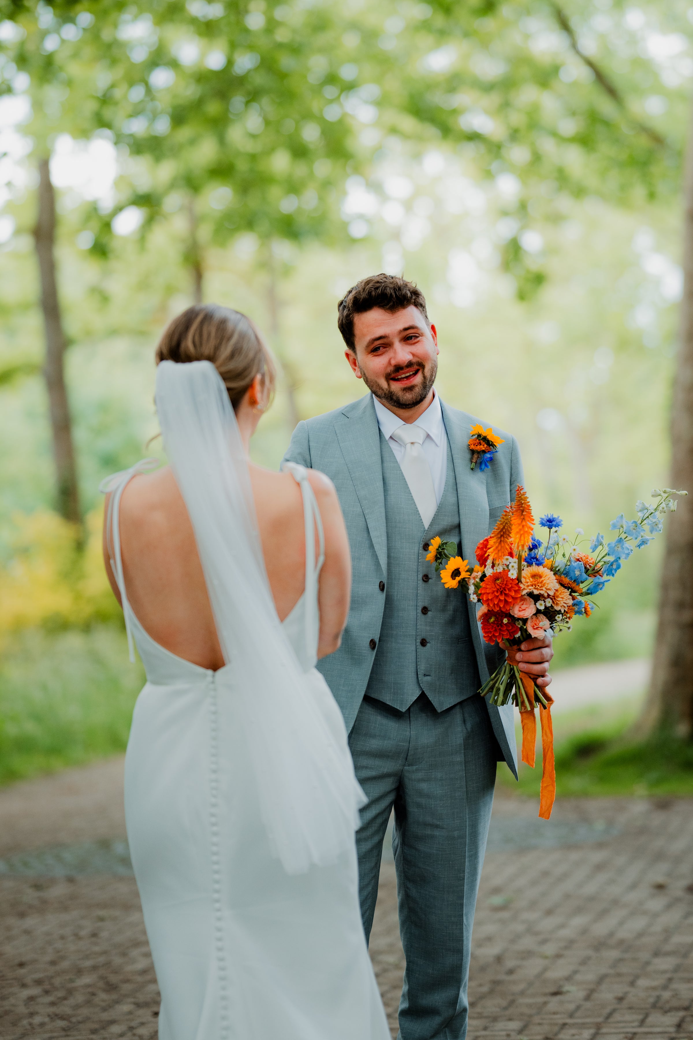 Groom holding a bouquet of flowers, standing next to a bride in a forest setting.